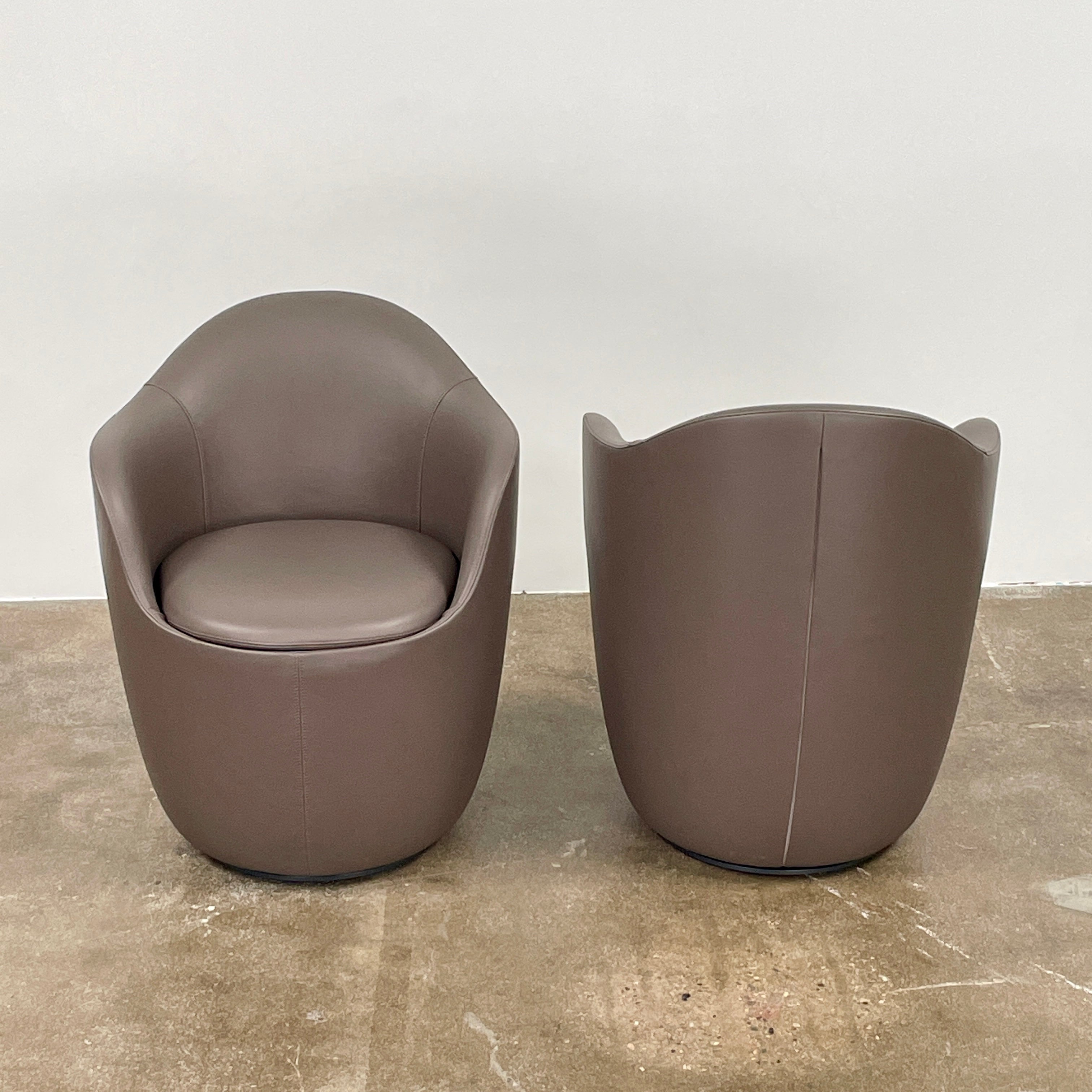 Two modern brown DWR Lina Swivel Dining Chairs with rounded backs and smooth upholstery, placed side by side on a white background.
