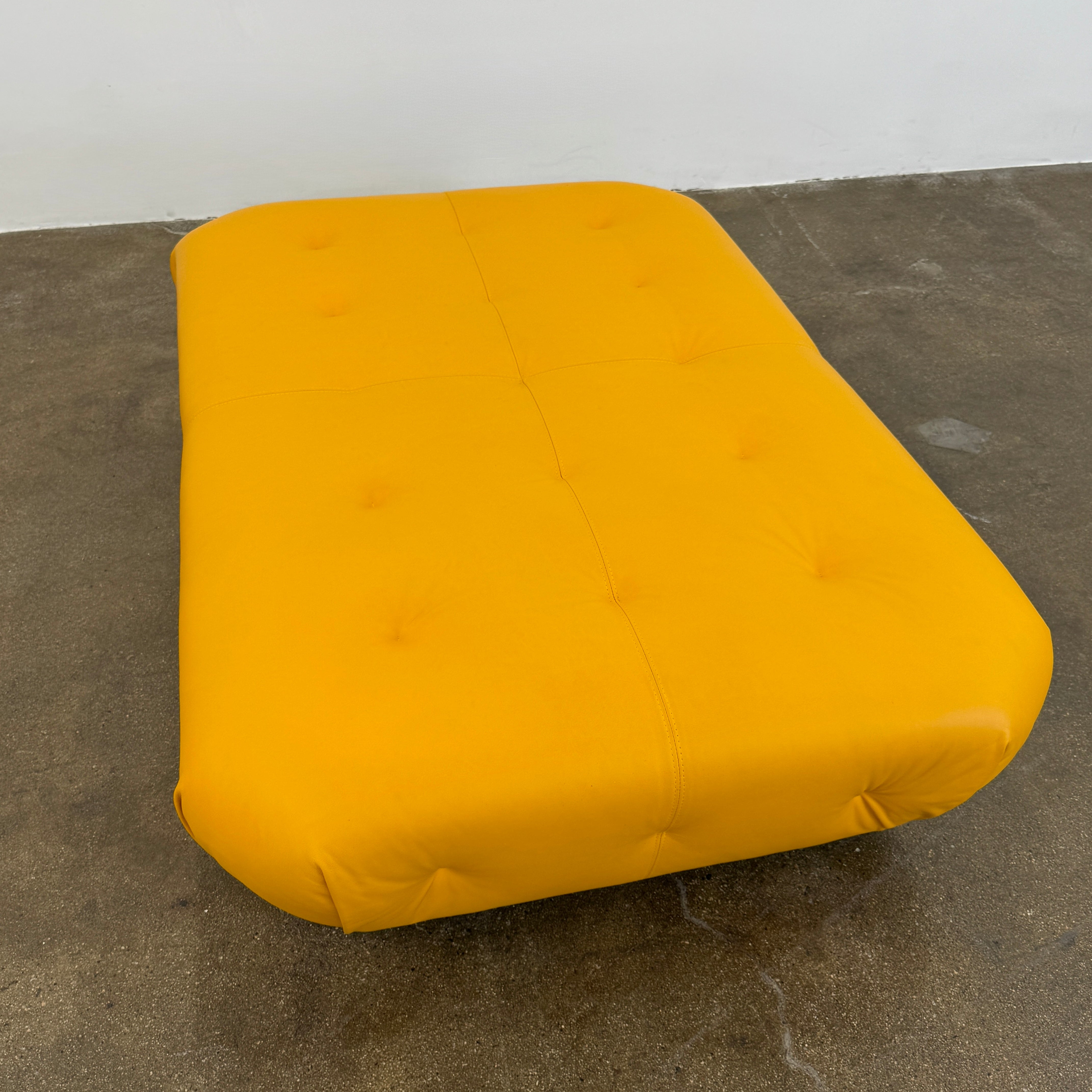 Yellow rectangular Tufted Leather Ottoman with rounded edges and a flat black base, ideal for extra seating, displayed on a plain white background. Brand: Unknown.