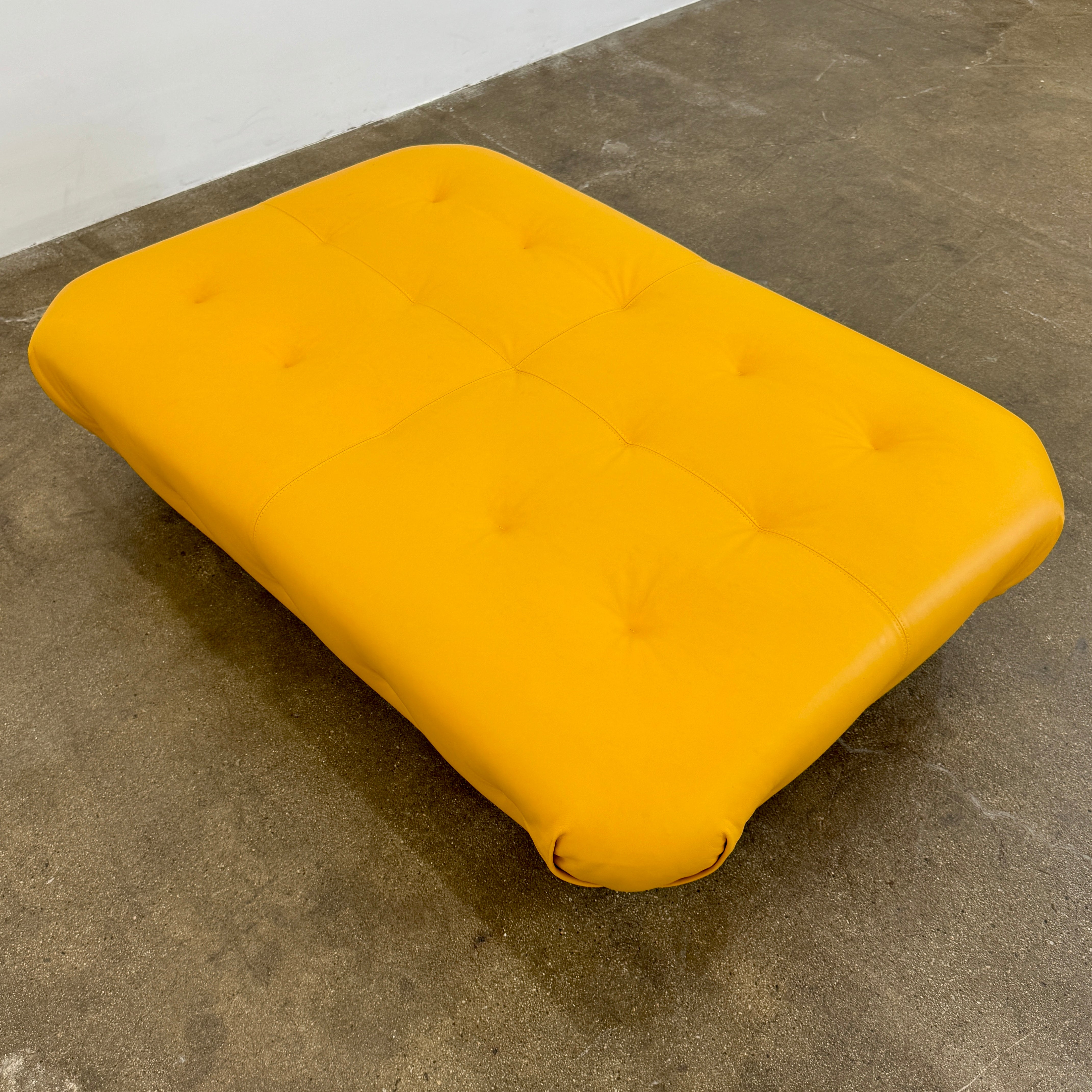 Yellow rectangular Tufted Leather Ottoman with rounded edges and a flat black base, ideal for extra seating, displayed on a plain white background. Brand: Unknown.