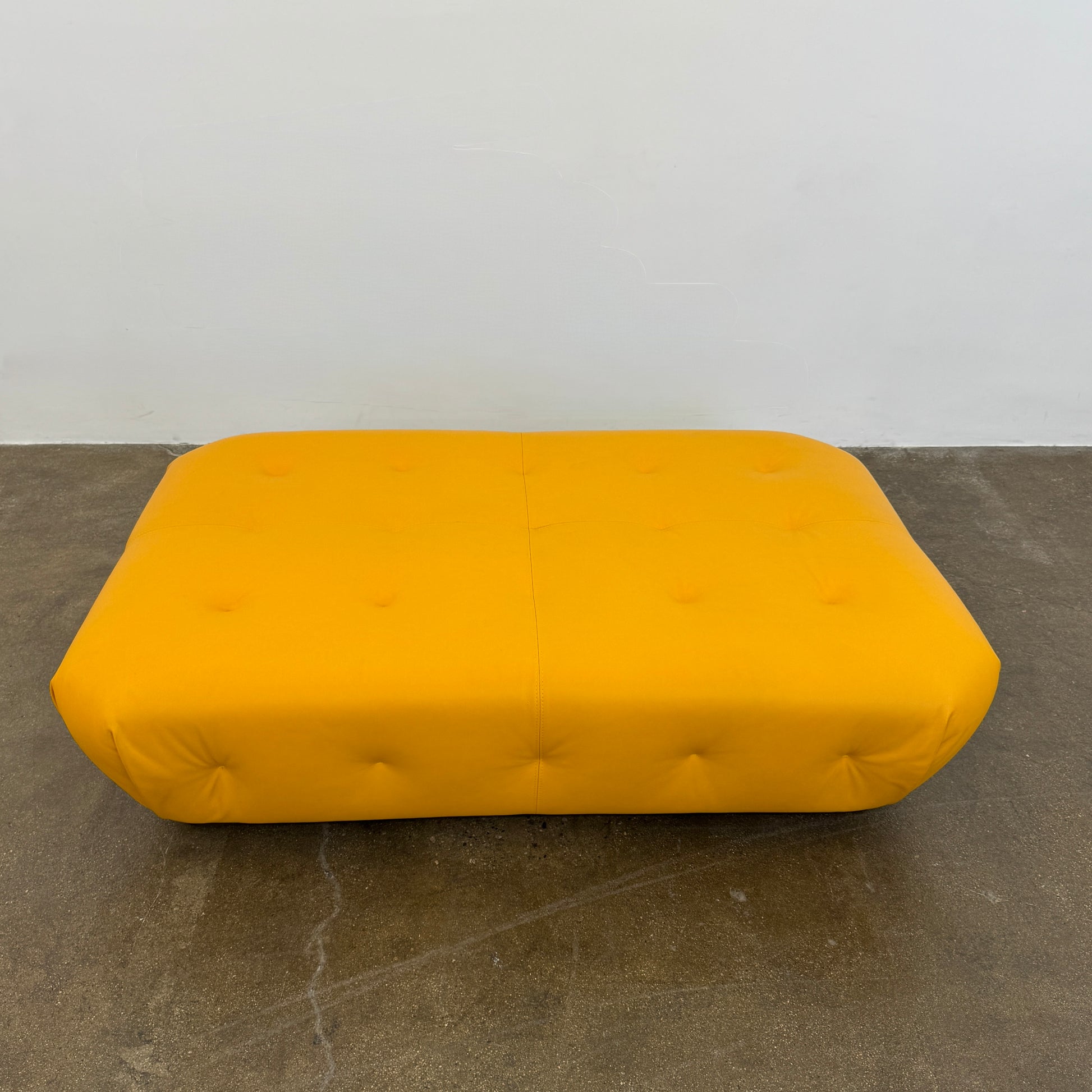 Yellow rectangular Tufted Leather Ottoman with rounded edges and a flat black base, ideal for extra seating, displayed on a plain white background. Brand: Unknown.