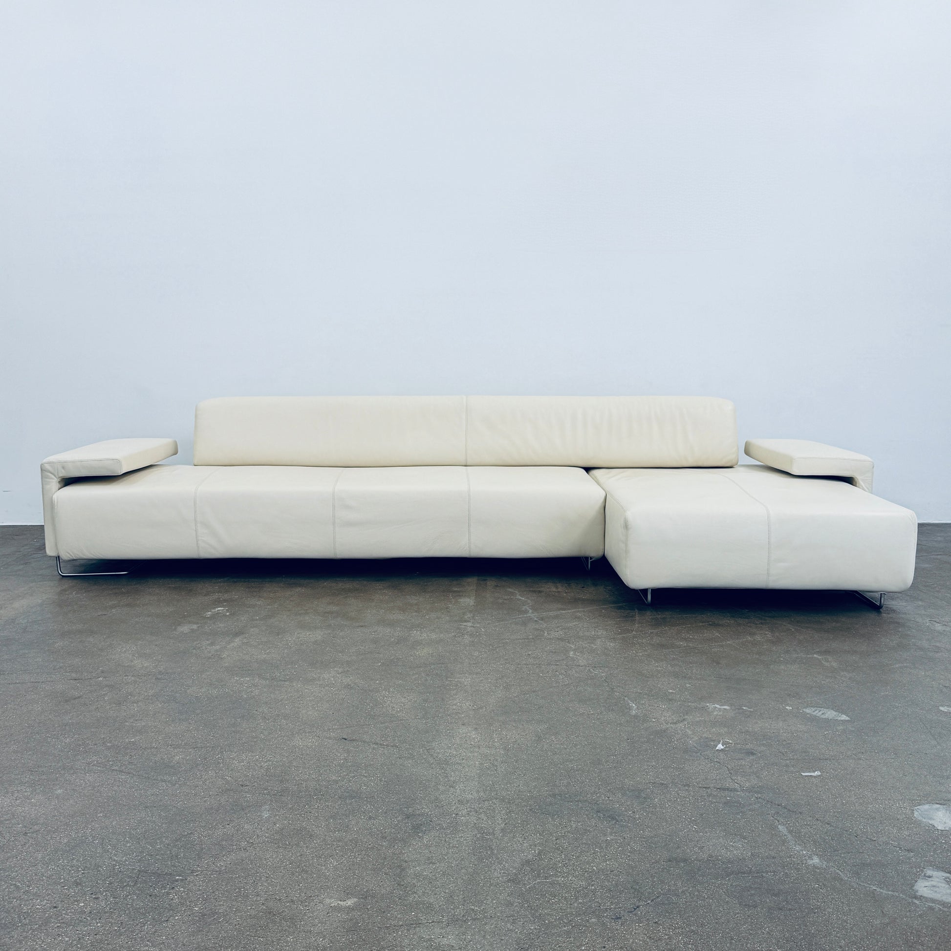 A Moroso Lowland Sectional Sofa in bone leather, with a right chaise lounge, stands on a bare concrete floor against a plain light wall.