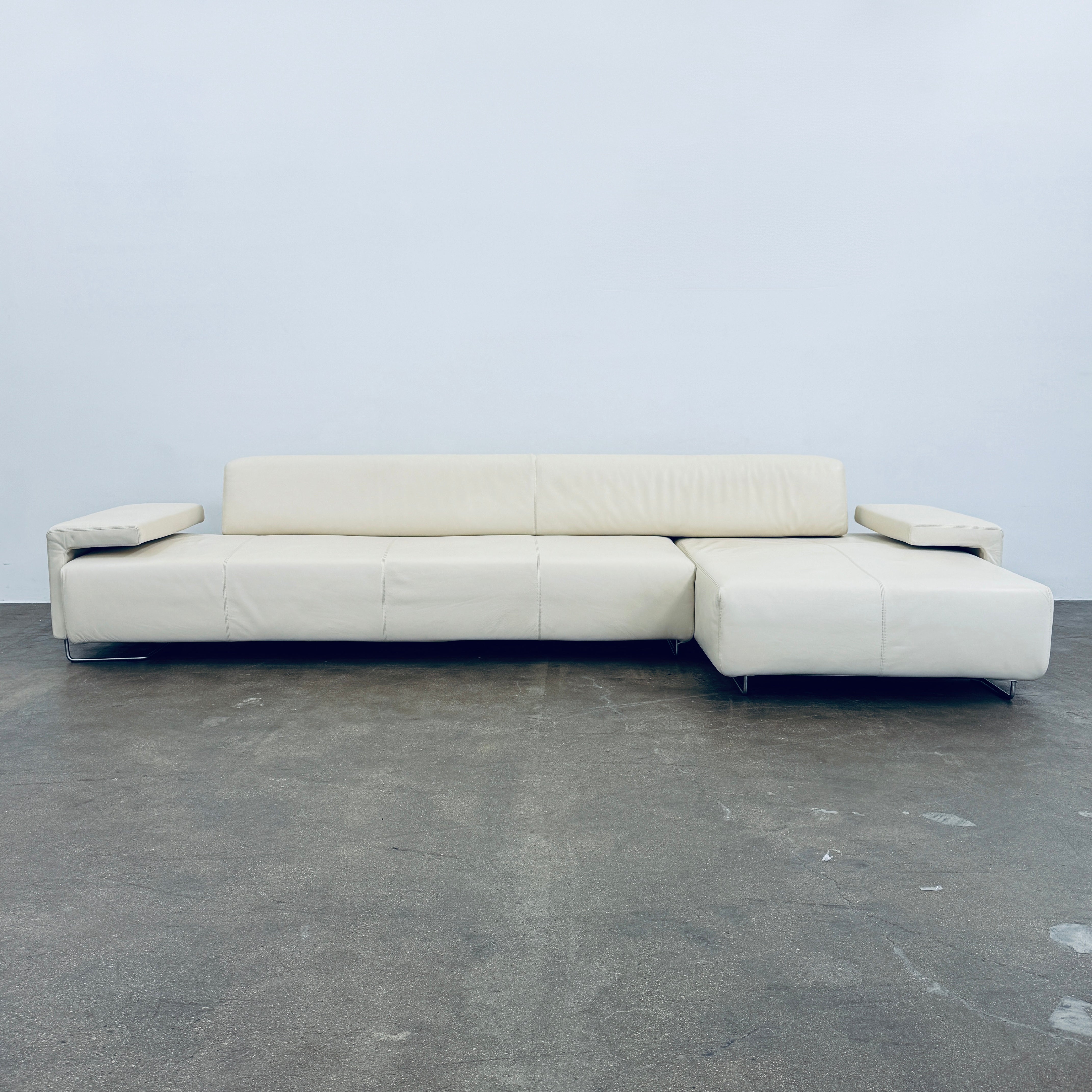 A Moroso Lowland Sectional Sofa in bone leather, with a right chaise lounge, stands on a bare concrete floor against a plain light wall.