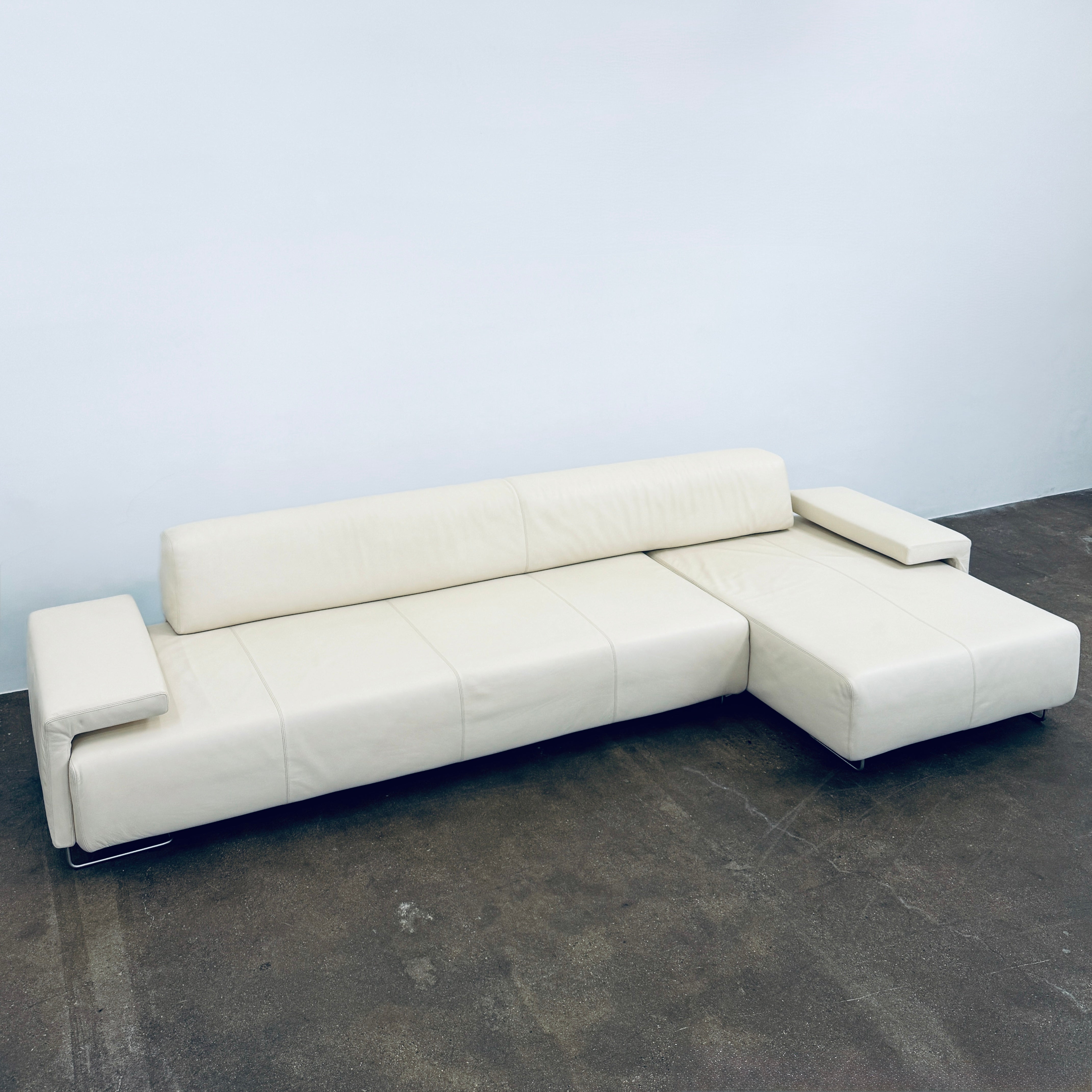 A Moroso Lowland Sectional Sofa in bone leather, with a right chaise lounge, stands on a bare concrete floor against a plain light wall.