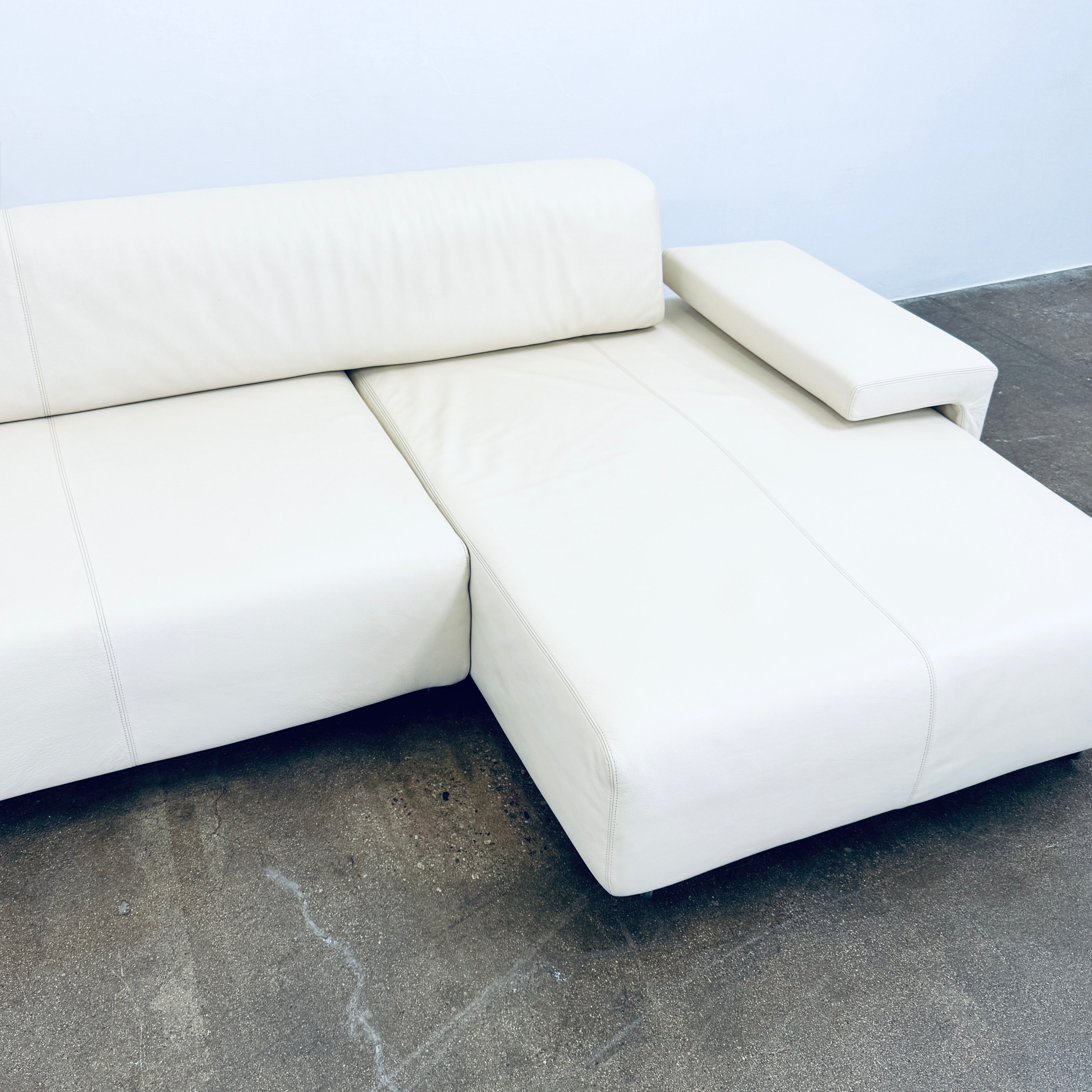 A Moroso Lowland Sectional Sofa in bone leather, with a right chaise lounge, stands on a bare concrete floor against a plain light wall.