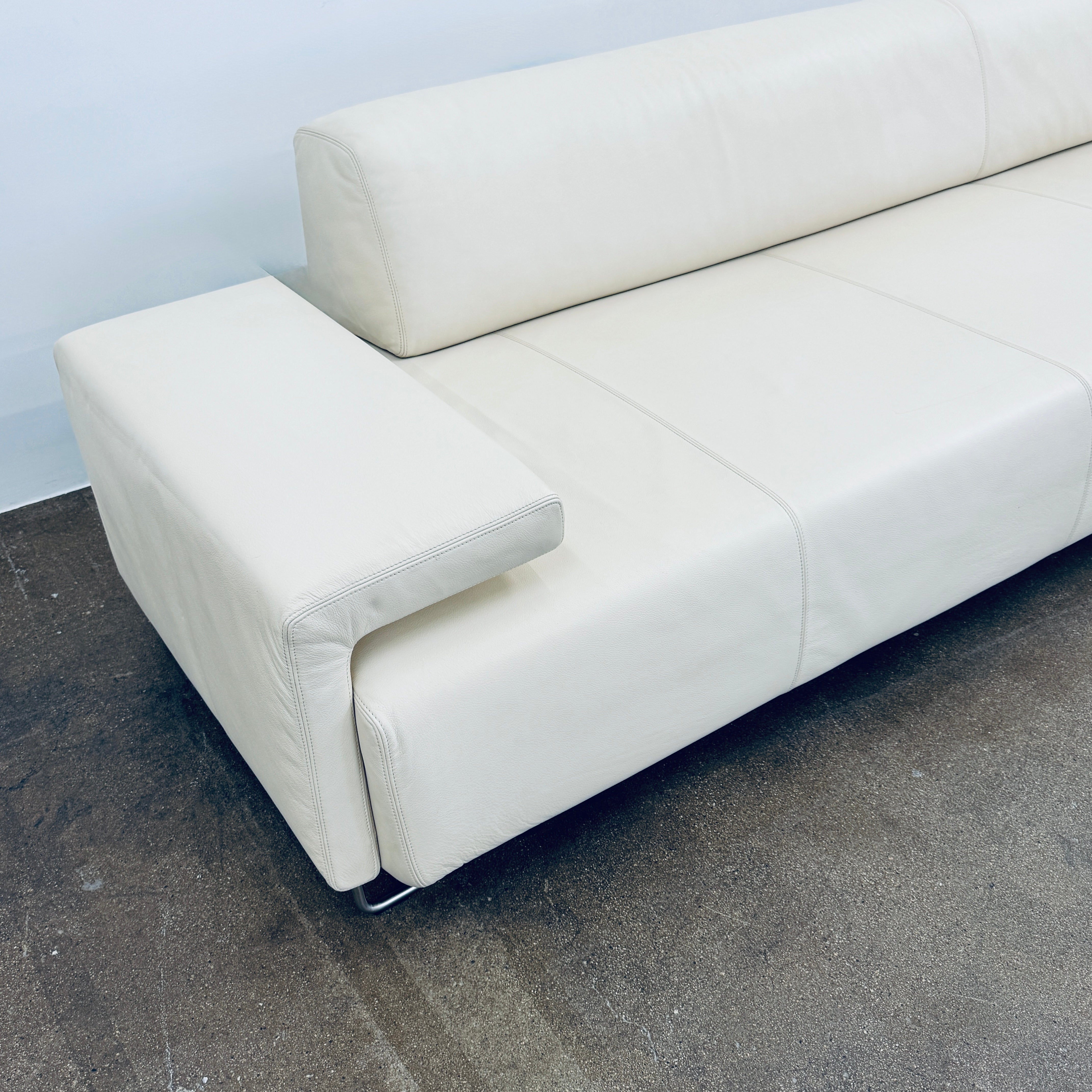 A Moroso Lowland Sectional Sofa in bone leather, with a right chaise lounge, stands on a bare concrete floor against a plain light wall.