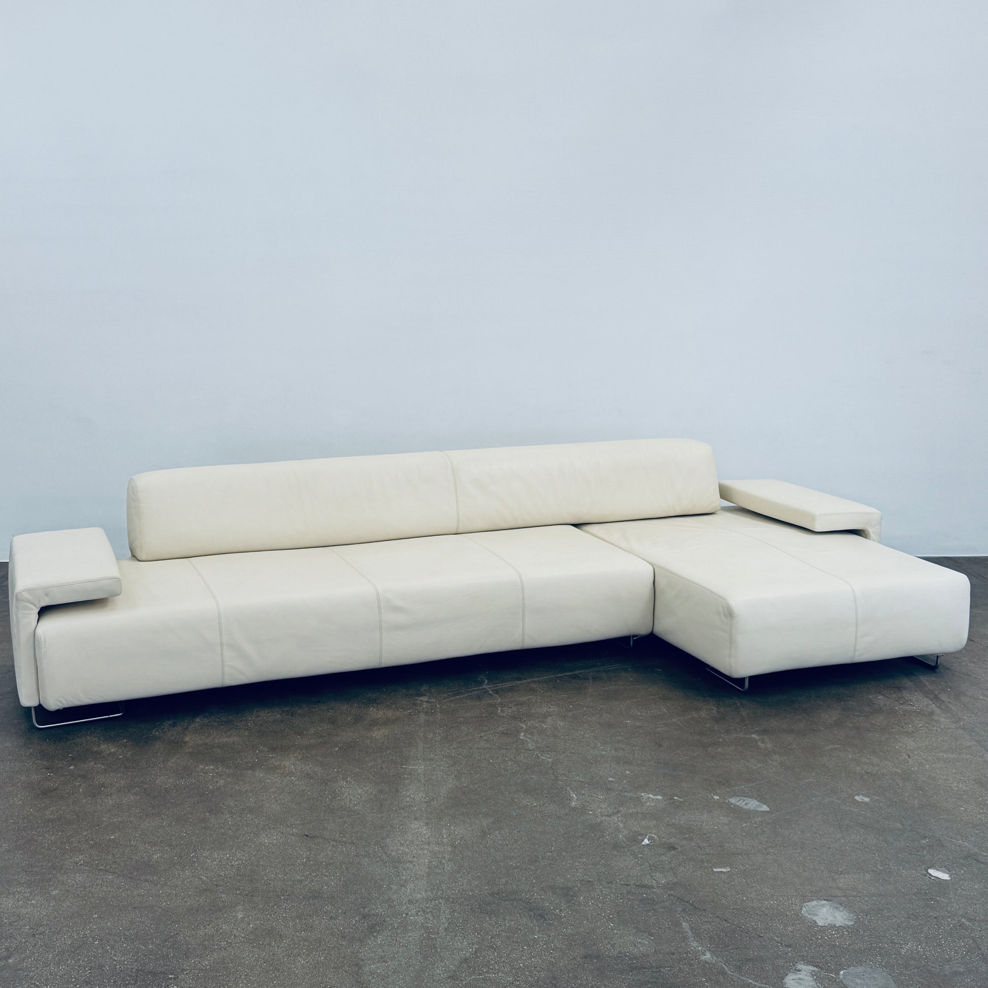 A Moroso Lowland Sectional Sofa in bone leather, with a right chaise lounge, stands on a bare concrete floor against a plain light wall.
