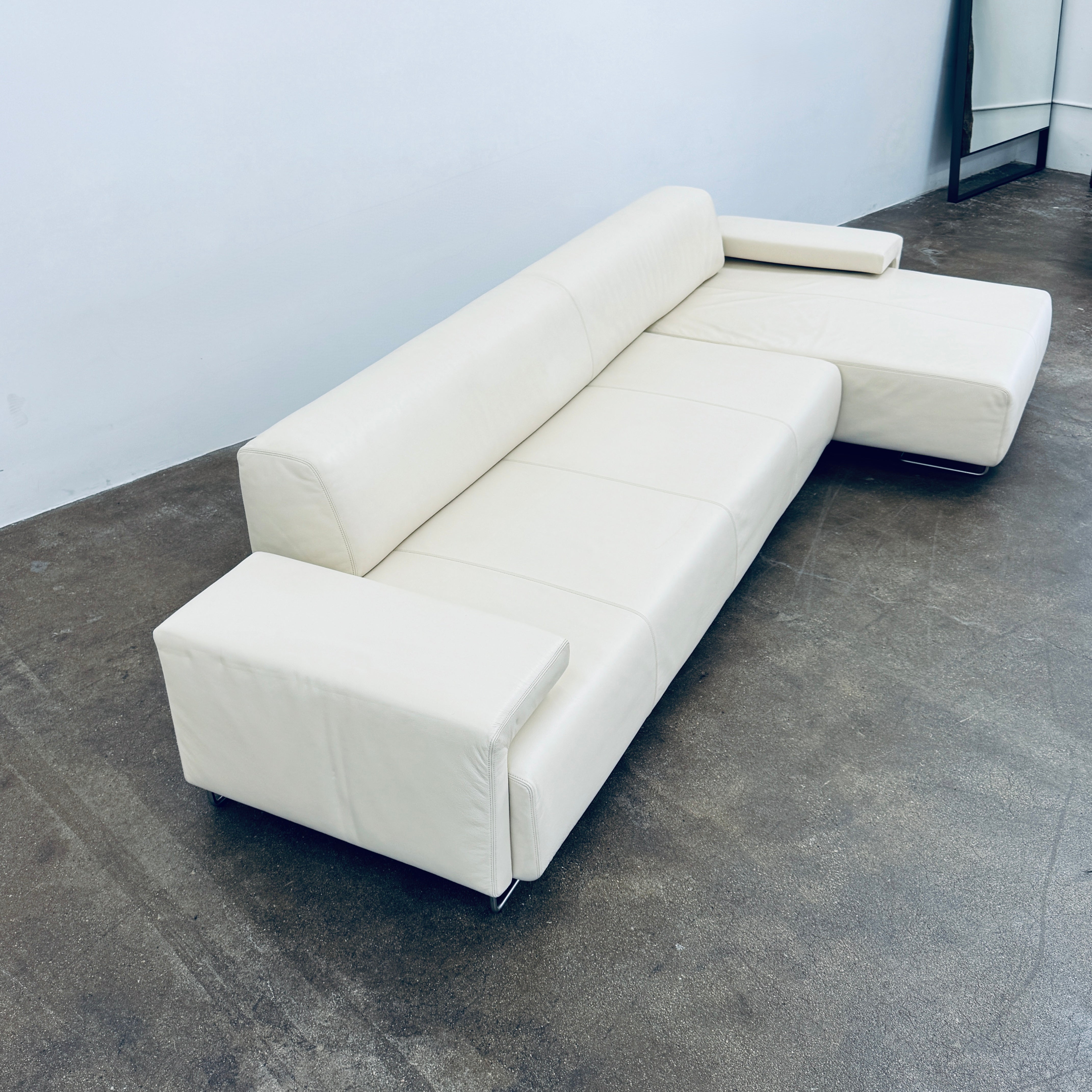 A Moroso Lowland Sectional Sofa in bone leather, with a right chaise lounge, stands on a bare concrete floor against a plain light wall.