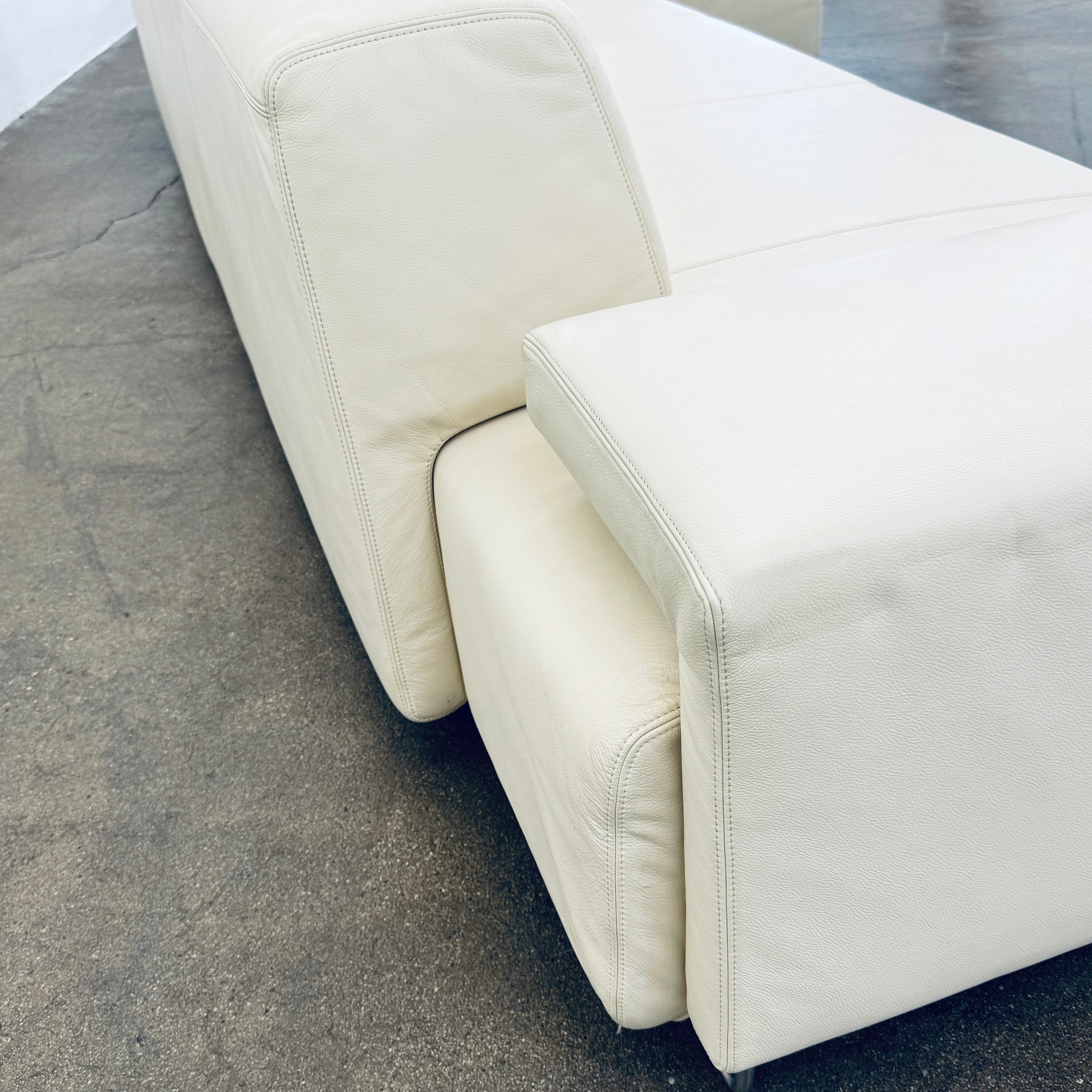 A Moroso Lowland Sectional Sofa in bone leather, with a right chaise lounge, stands on a bare concrete floor against a plain light wall.