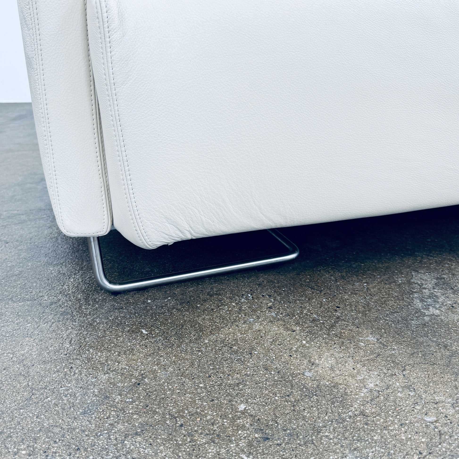 A Moroso Lowland Sectional Sofa in bone leather, with a right chaise lounge, stands on a bare concrete floor against a plain light wall.