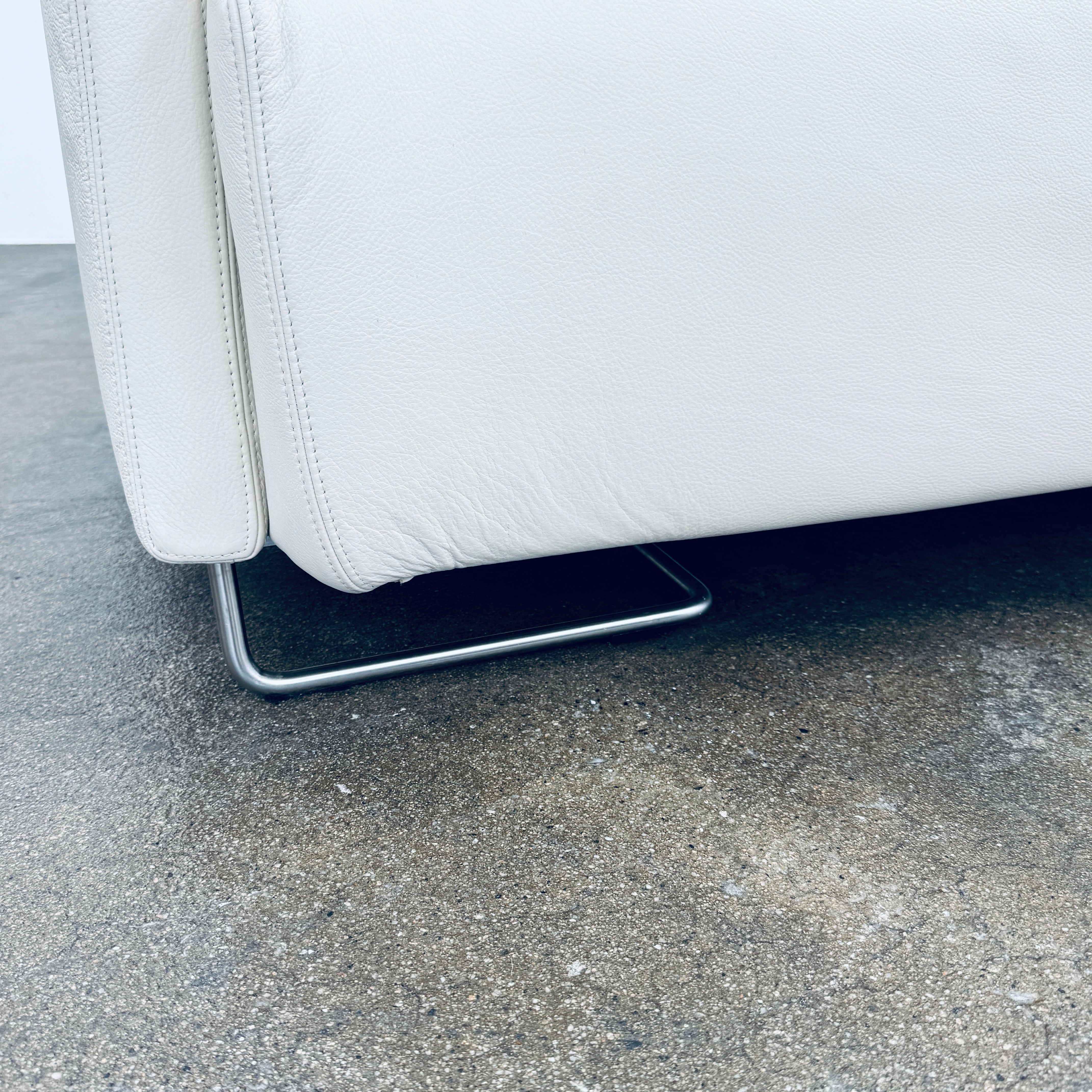 A Moroso Lowland Sectional Sofa in bone leather, with a right chaise lounge, stands on a bare concrete floor against a plain light wall.