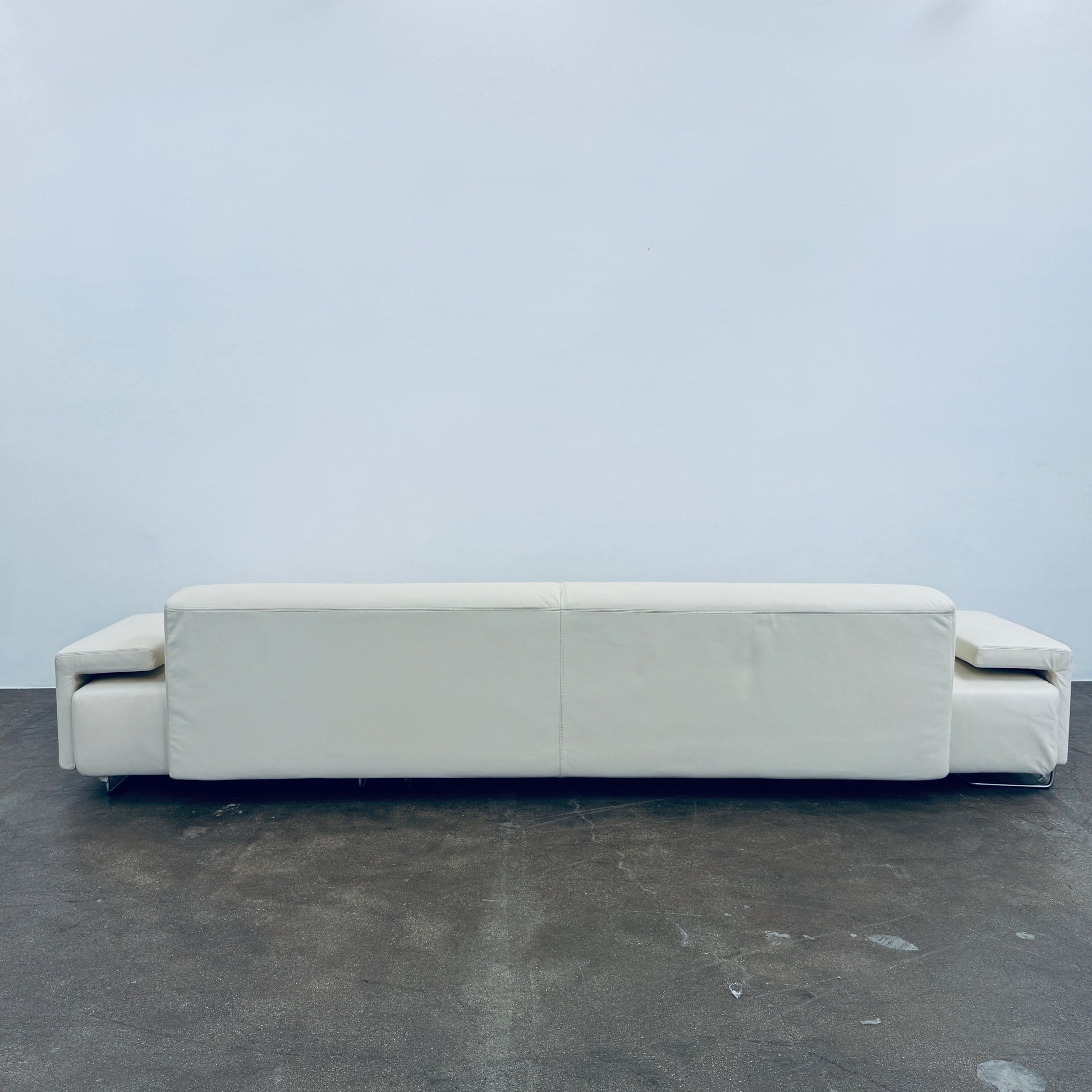 A Moroso Lowland Sectional Sofa in bone leather, with a right chaise lounge, stands on a bare concrete floor against a plain light wall.