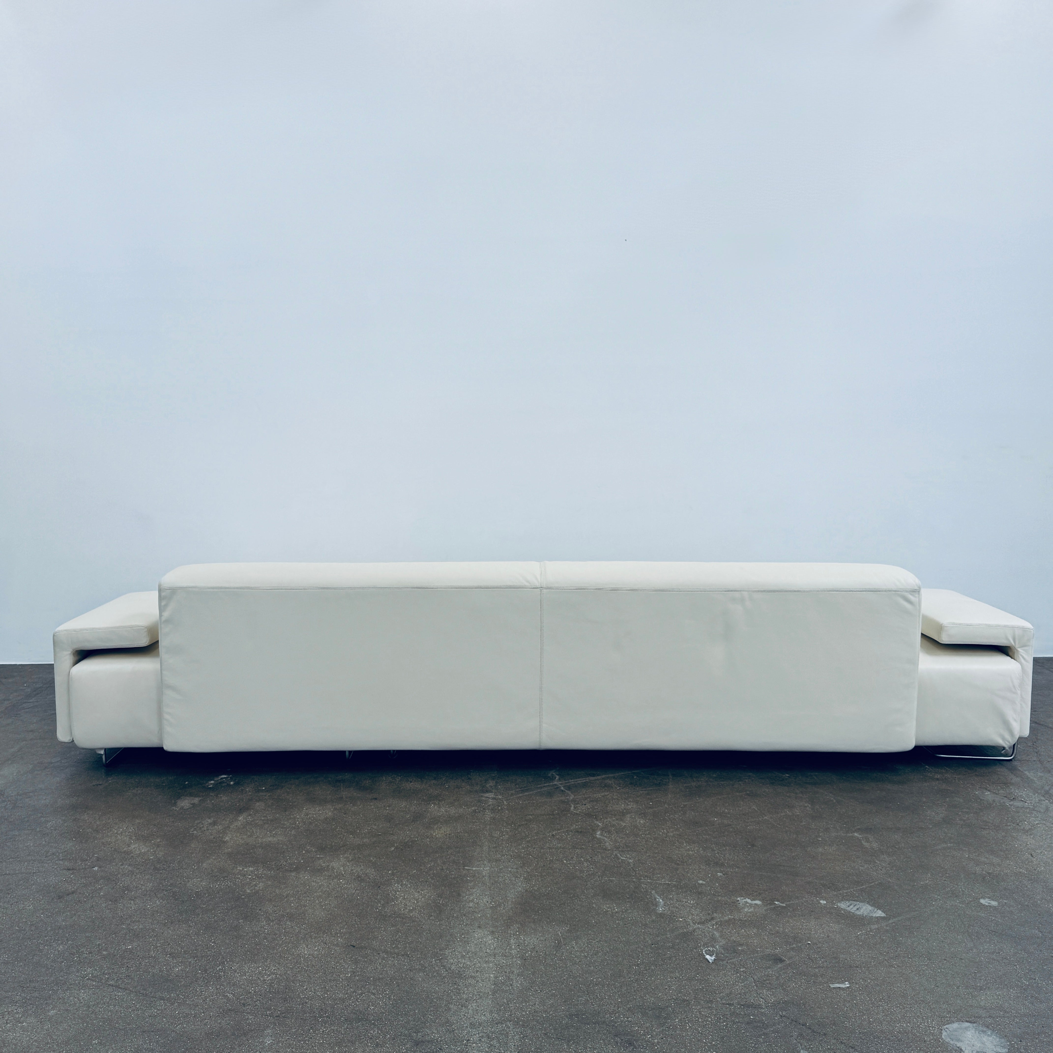 A Moroso Lowland Sectional Sofa in bone leather, with a right chaise lounge, stands on a bare concrete floor against a plain light wall.