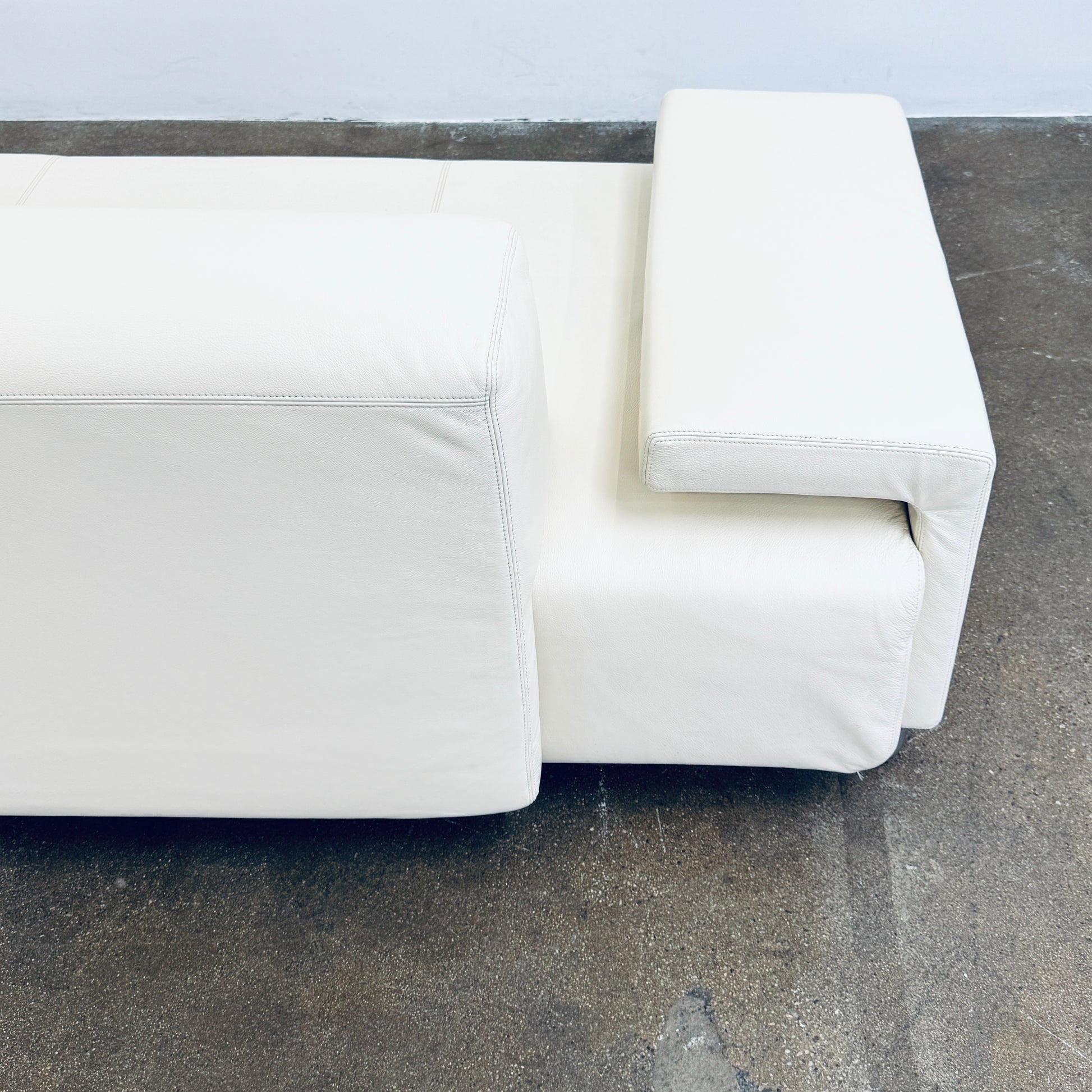 A Moroso Lowland Sectional Sofa in bone leather, with a right chaise lounge, stands on a bare concrete floor against a plain light wall.