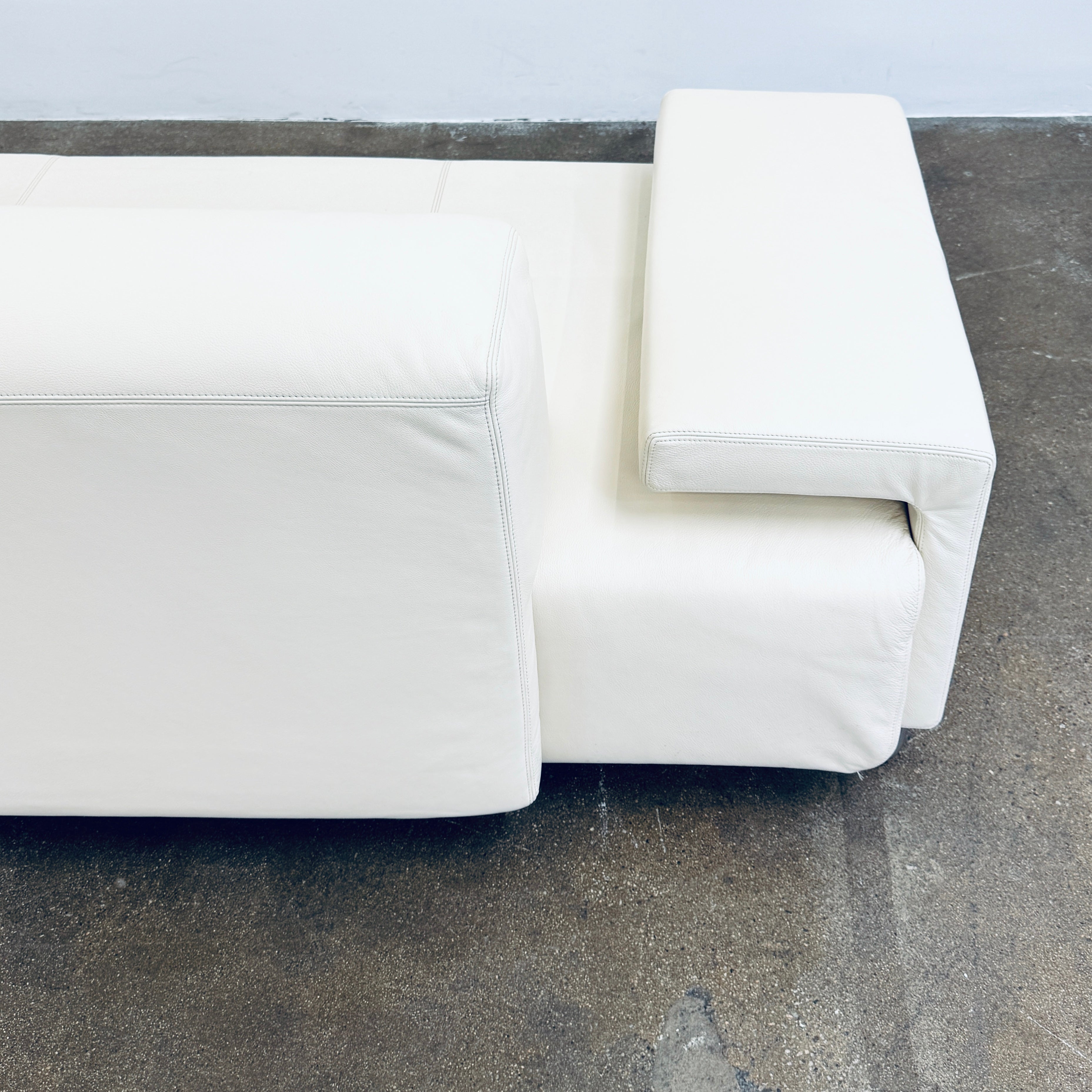 A Moroso Lowland Sectional Sofa in bone leather, with a right chaise lounge, stands on a bare concrete floor against a plain light wall.