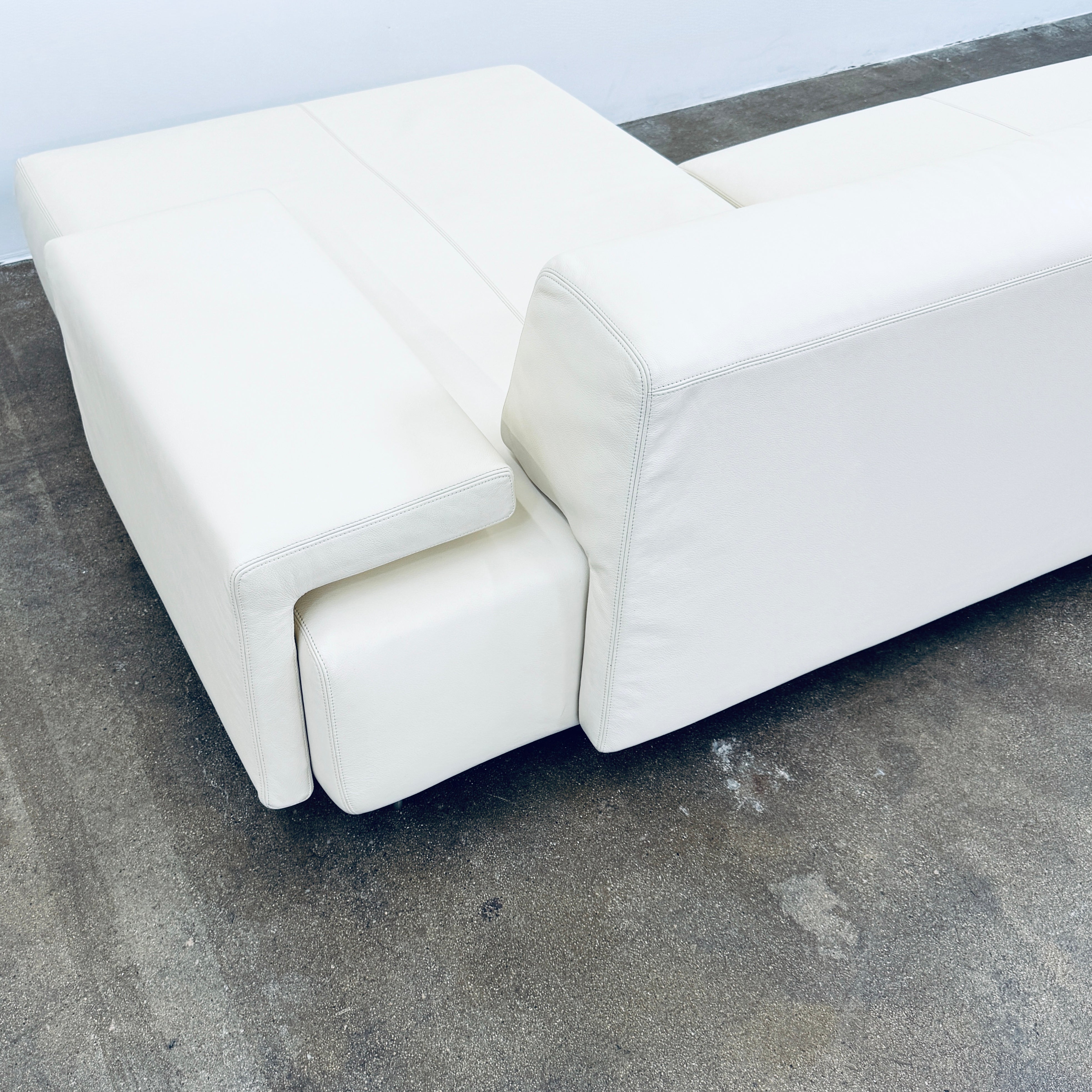 A Moroso Lowland Sectional Sofa in bone leather, with a right chaise lounge, stands on a bare concrete floor against a plain light wall.