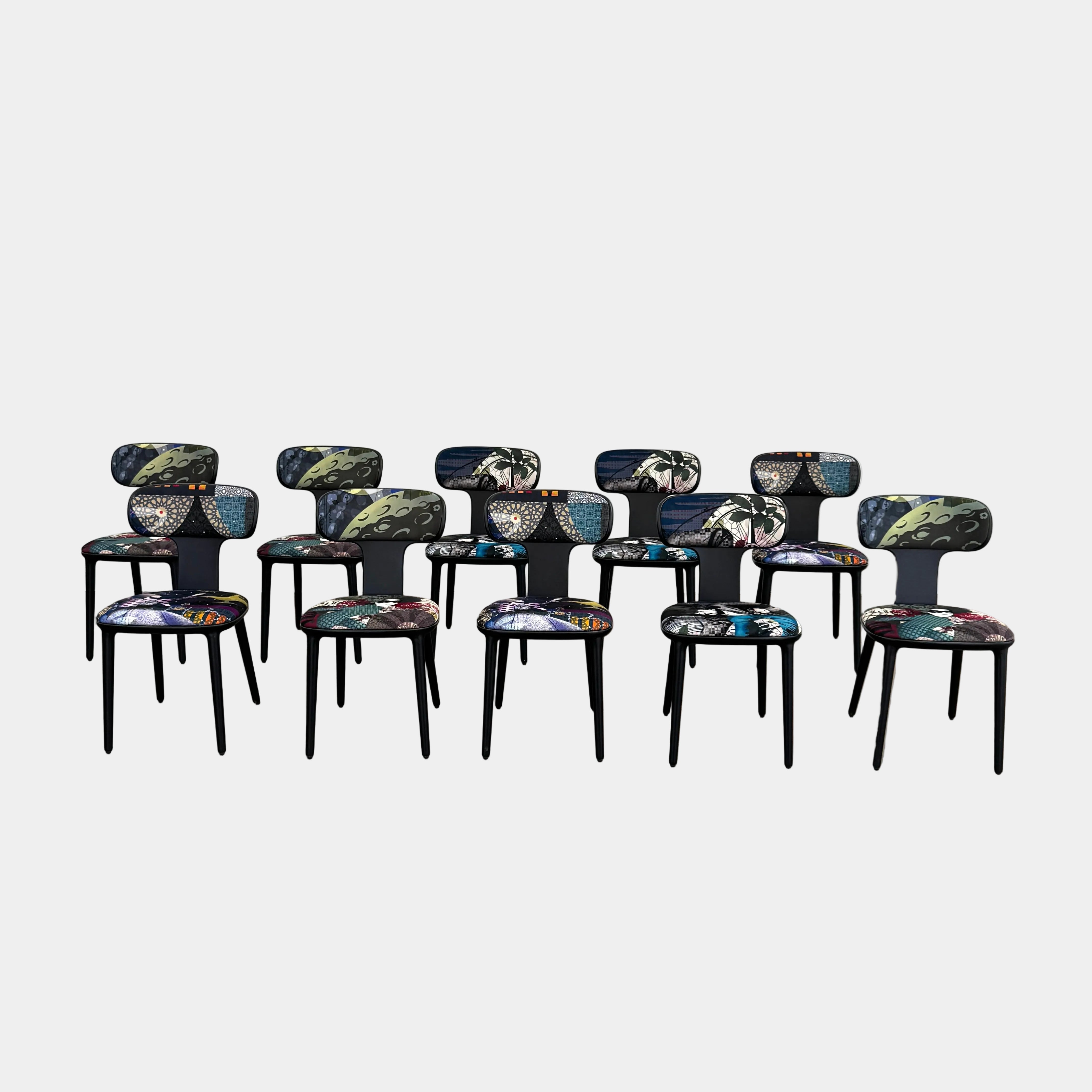 A set of 10 Roche Bobois Globe Trotter Operette Dining Chairs, featuring colorful patterned upholstery, is arranged on a polished concrete floor against a plain white wall.