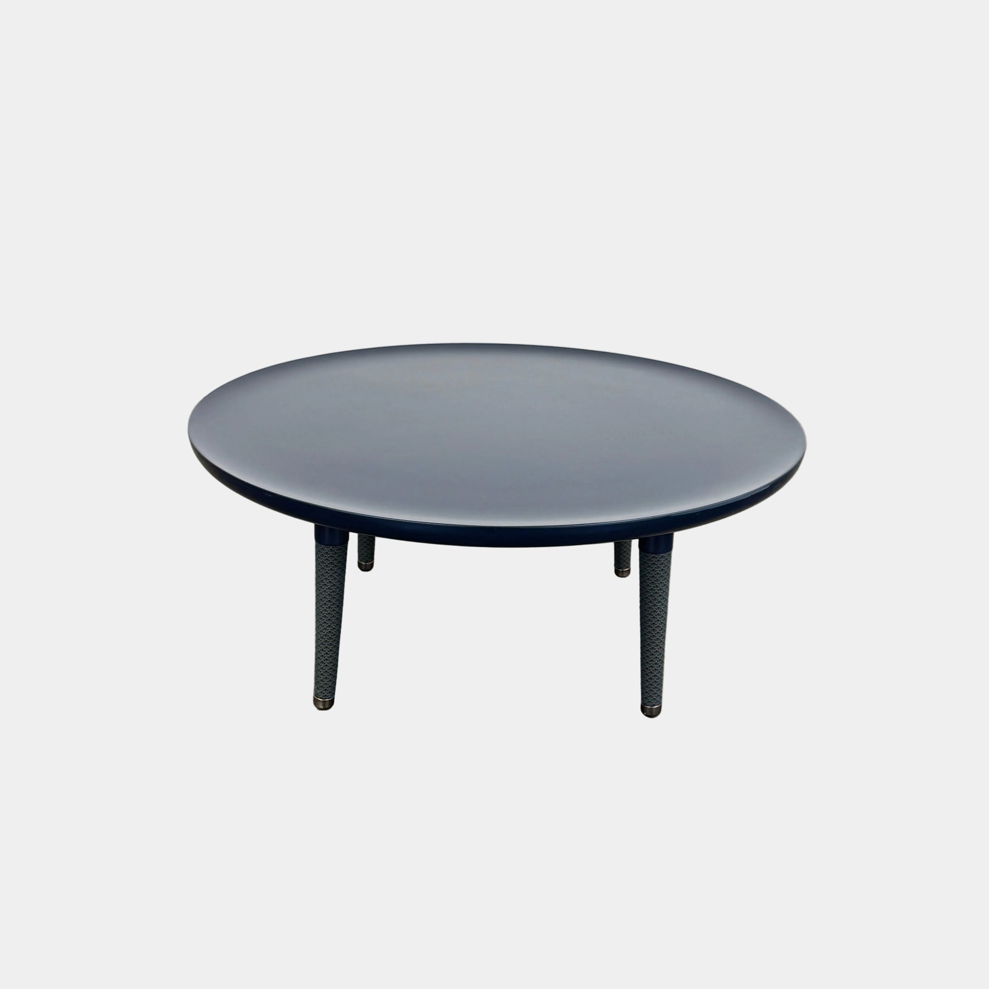 The Roche Bobois Globe Trotter La Parisienne cocktail table features a round, dark blue top and three textured legs, shown against a light gray background.