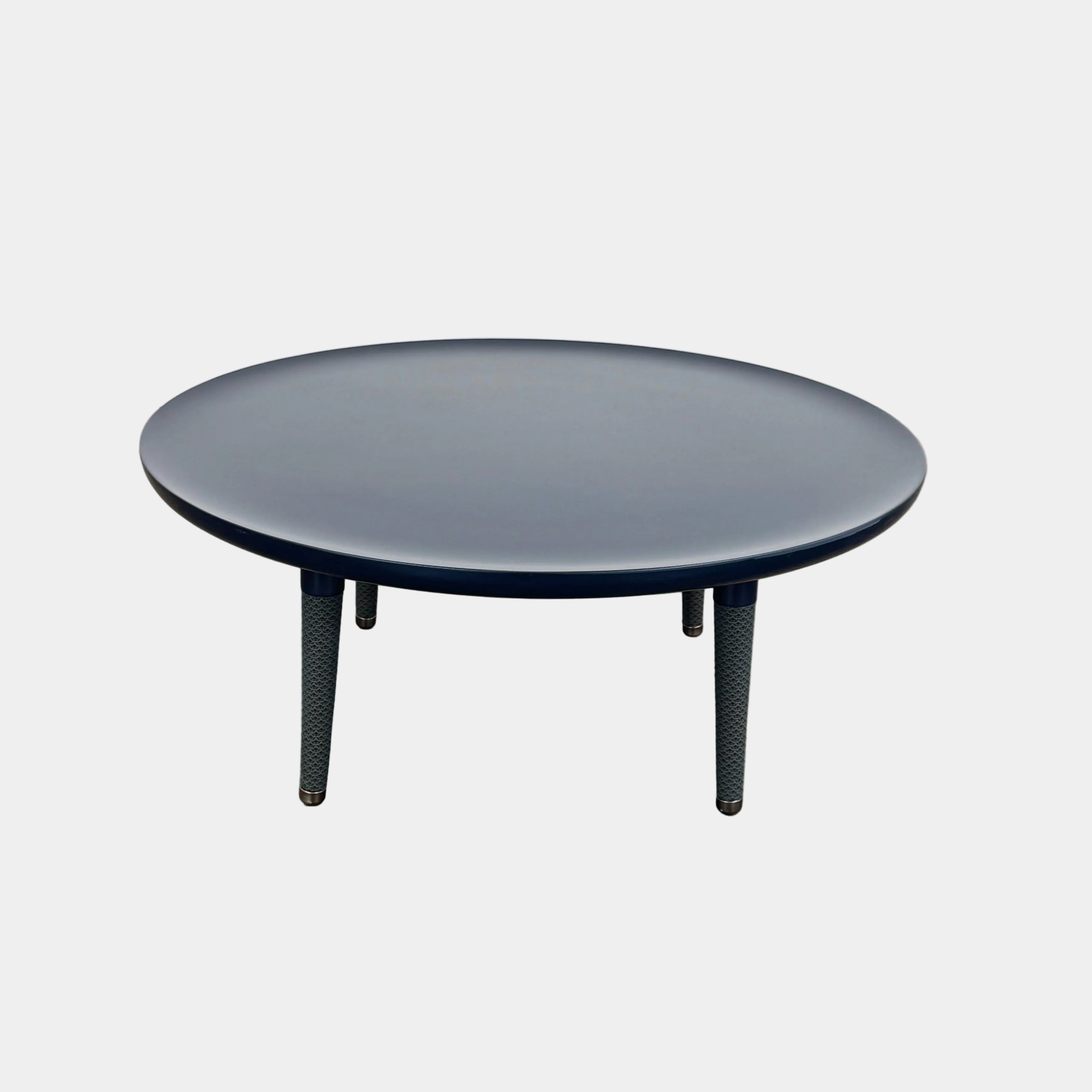 The Roche Bobois Globe Trotter La Parisienne cocktail table features a round, dark blue top and three textured legs, shown against a light gray background.