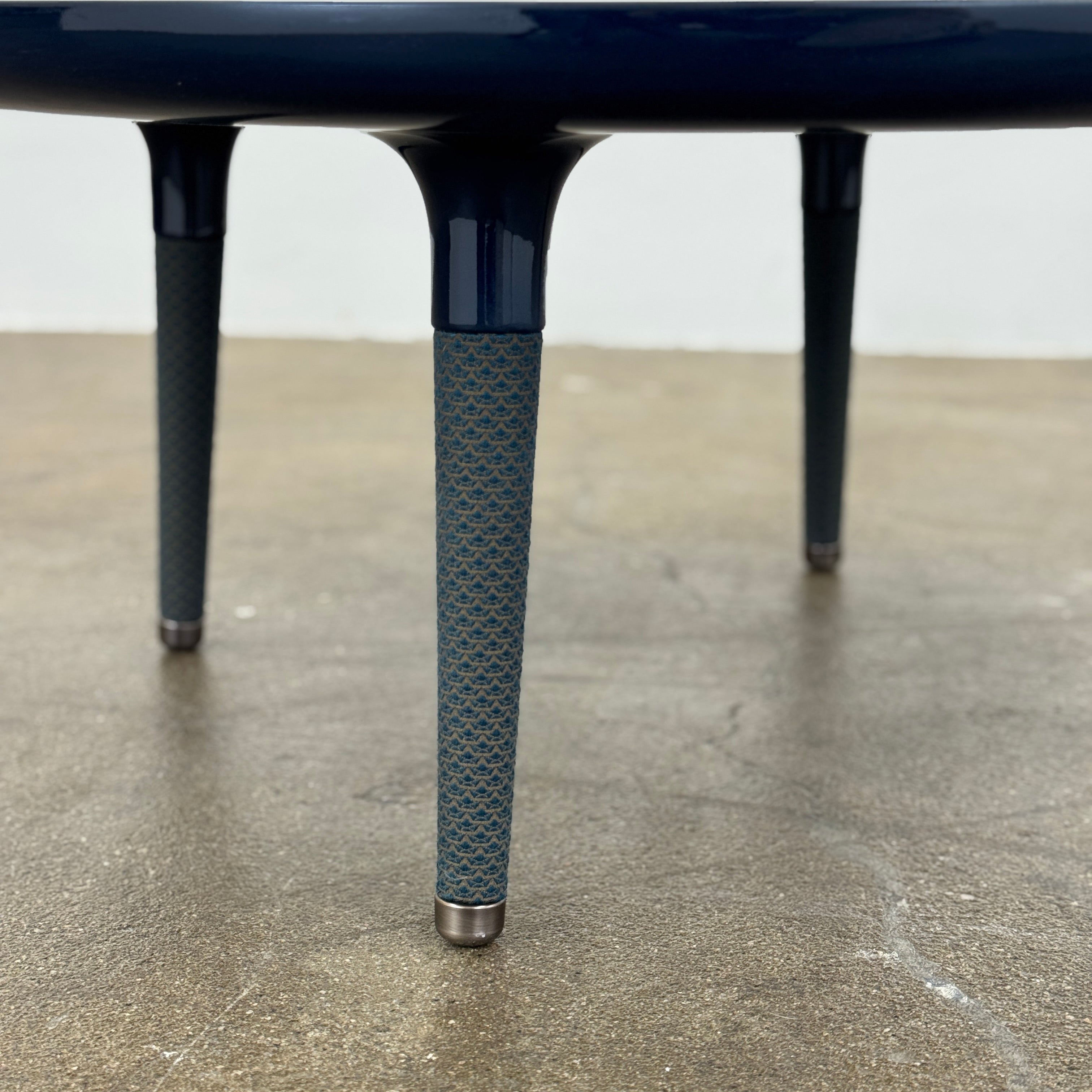 The Roche Bobois Globe Trotter La Parisienne cocktail table features a round, dark blue top and three textured legs, shown against a light gray background.