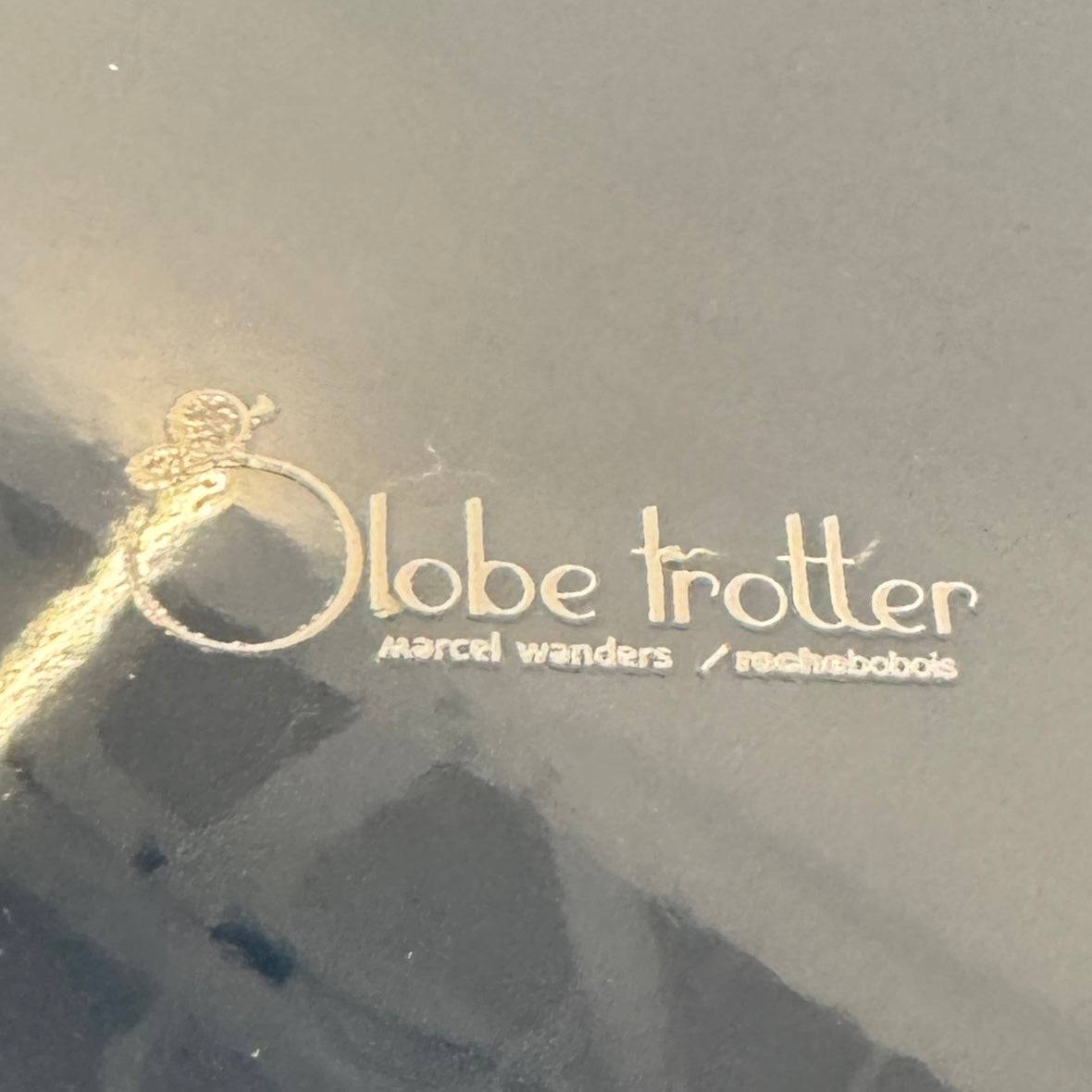 The Roche Bobois Globe Trotter La Parisienne cocktail table features a round, dark blue top and three textured legs, shown against a light gray background.