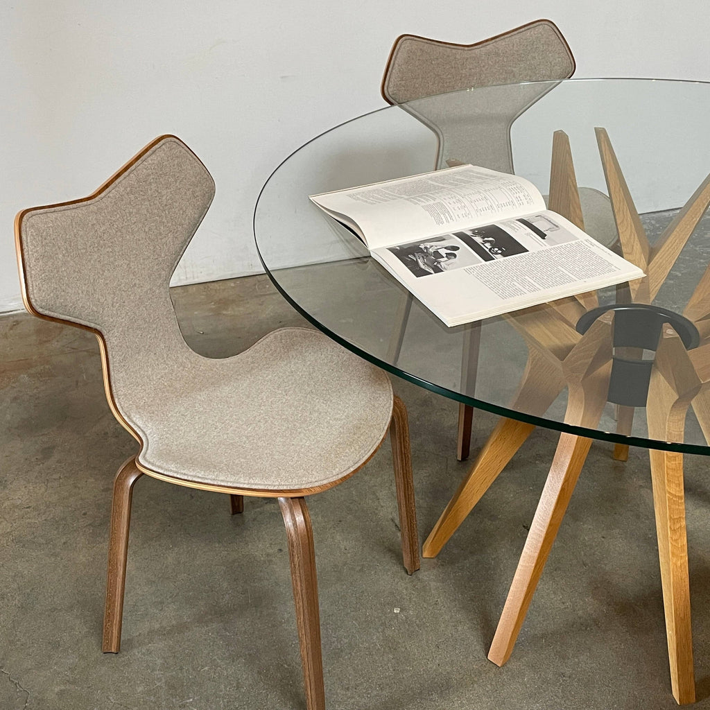 A modern dining set featuring a round glass table and the Fritz Hansen Grand Prix Chair Set with upholstered seats on a concrete floor.
