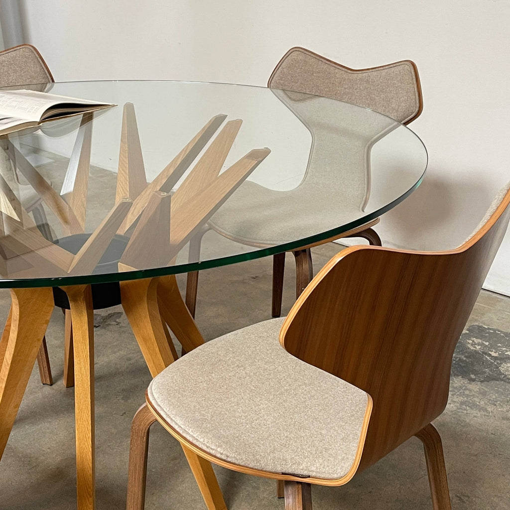 A modern dining set featuring a round glass table and the Fritz Hansen Grand Prix Chair Set with upholstered seats on a concrete floor.