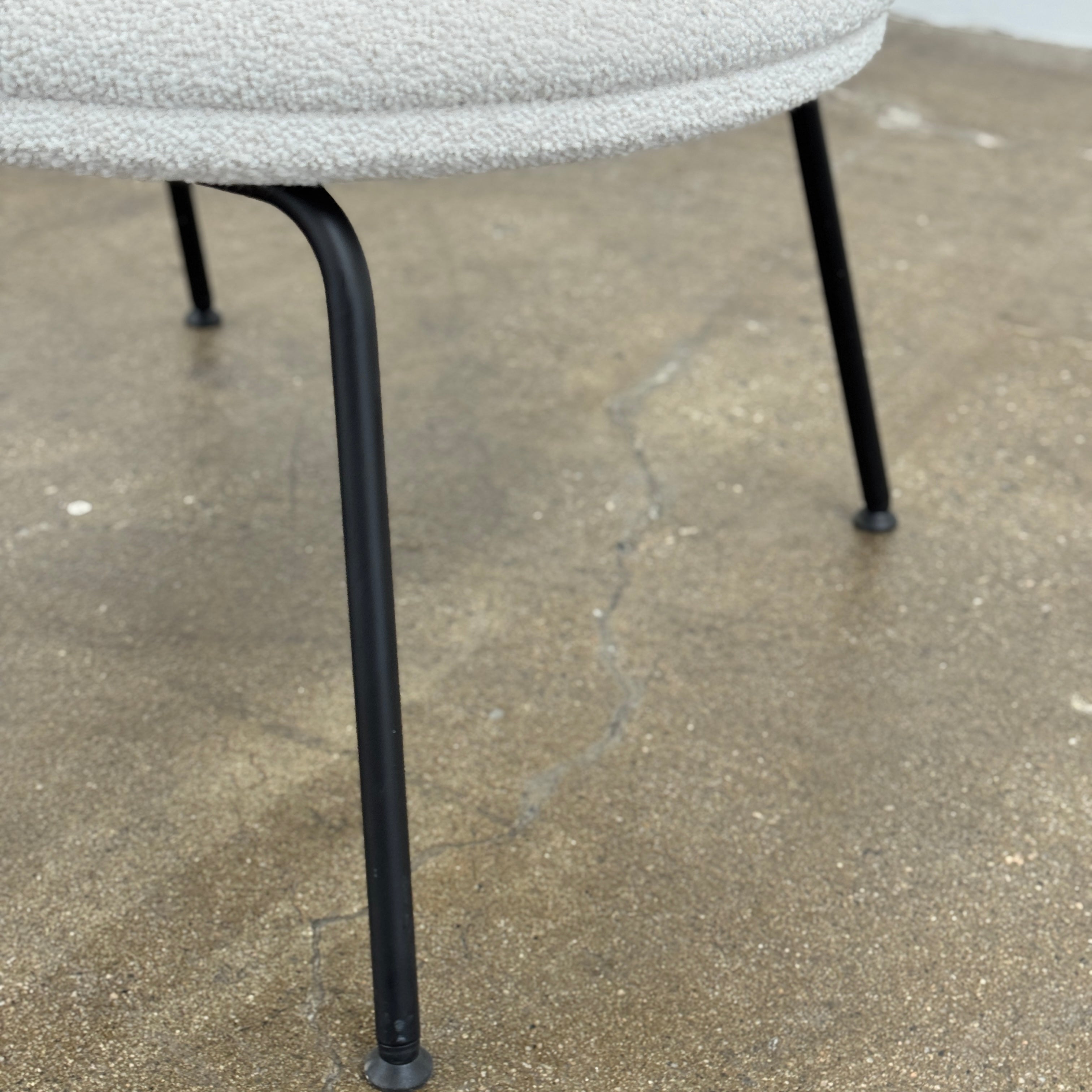 Two Arrmet Belle Lounge chairs by Arrmet, featuring white cushions, rounded backs, and black metal legs, are placed side by side on a brown concrete floor against a plain light gray wall.