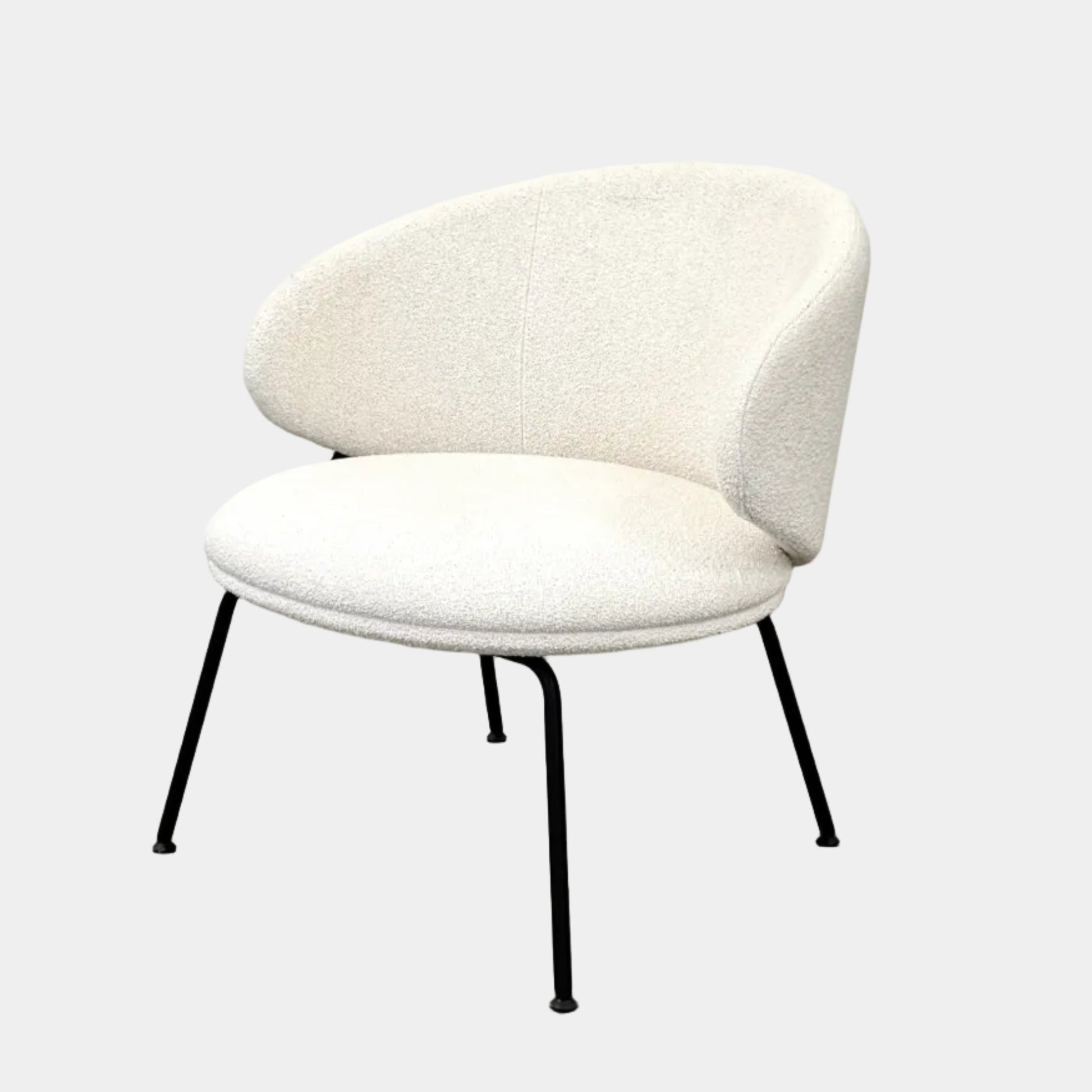 Two Arrmet Belle Lounge chairs by Arrmet, featuring white cushions, rounded backs, and black metal legs, are placed side by side on a brown concrete floor against a plain light gray wall.