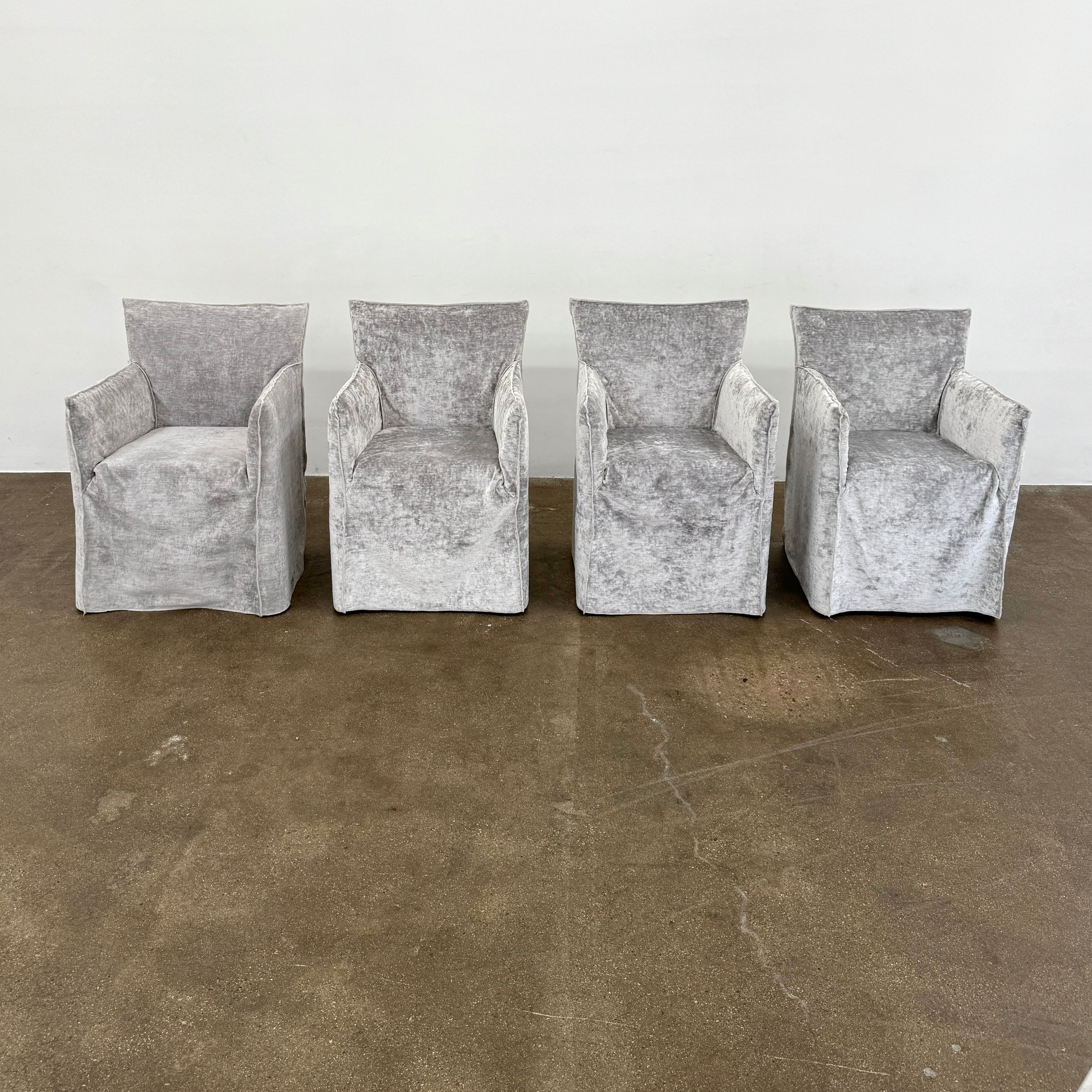 Four Gervasoni Ghost 25 Dining Armchairs by Gervasoni, featuring straight backs and skirted slipcovers in silver velvet, are arranged side by side against a white background for an elegant look.