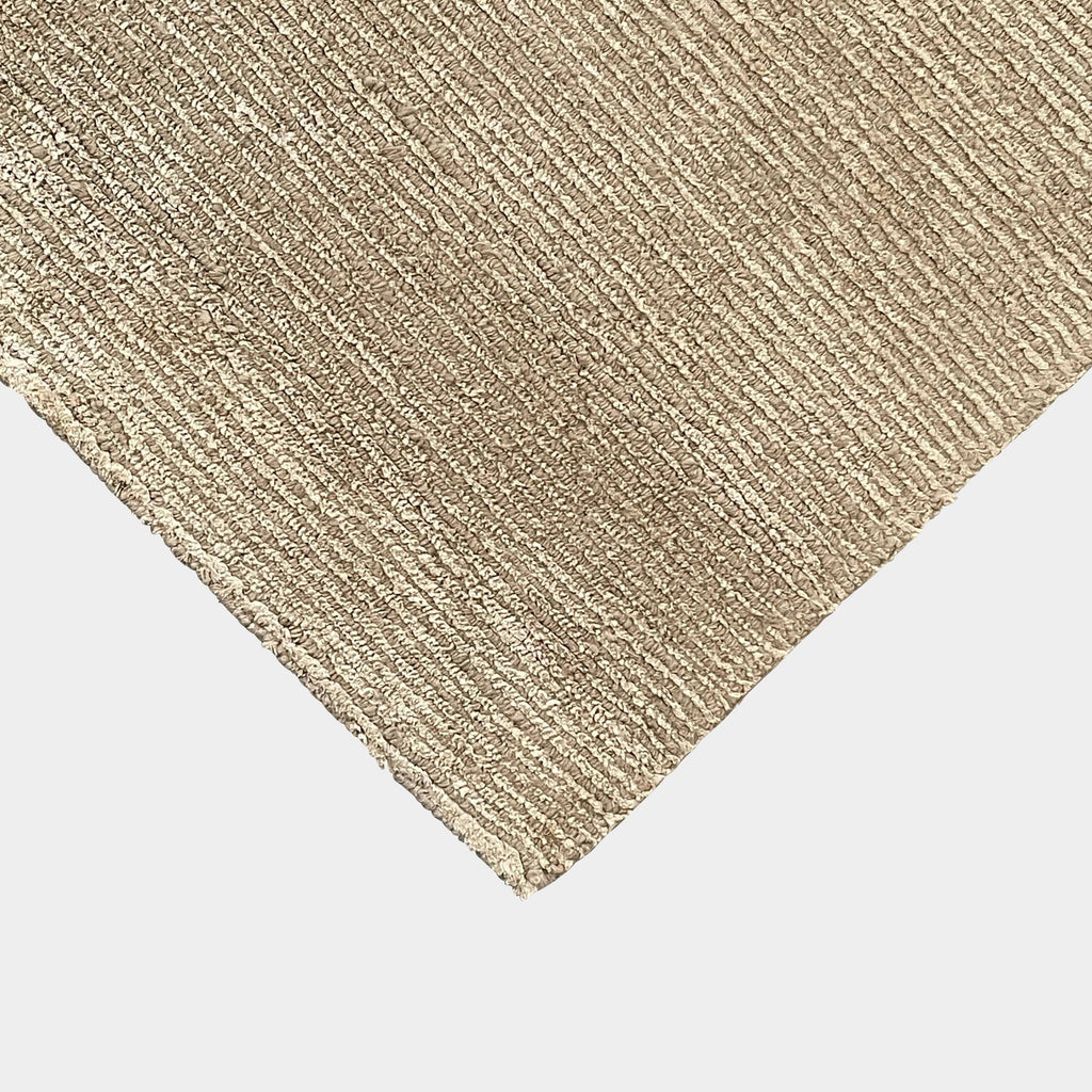 A close-up of a Delinear beige, hand-knotted textured carpet with a corner folded over, displayed against a white background.