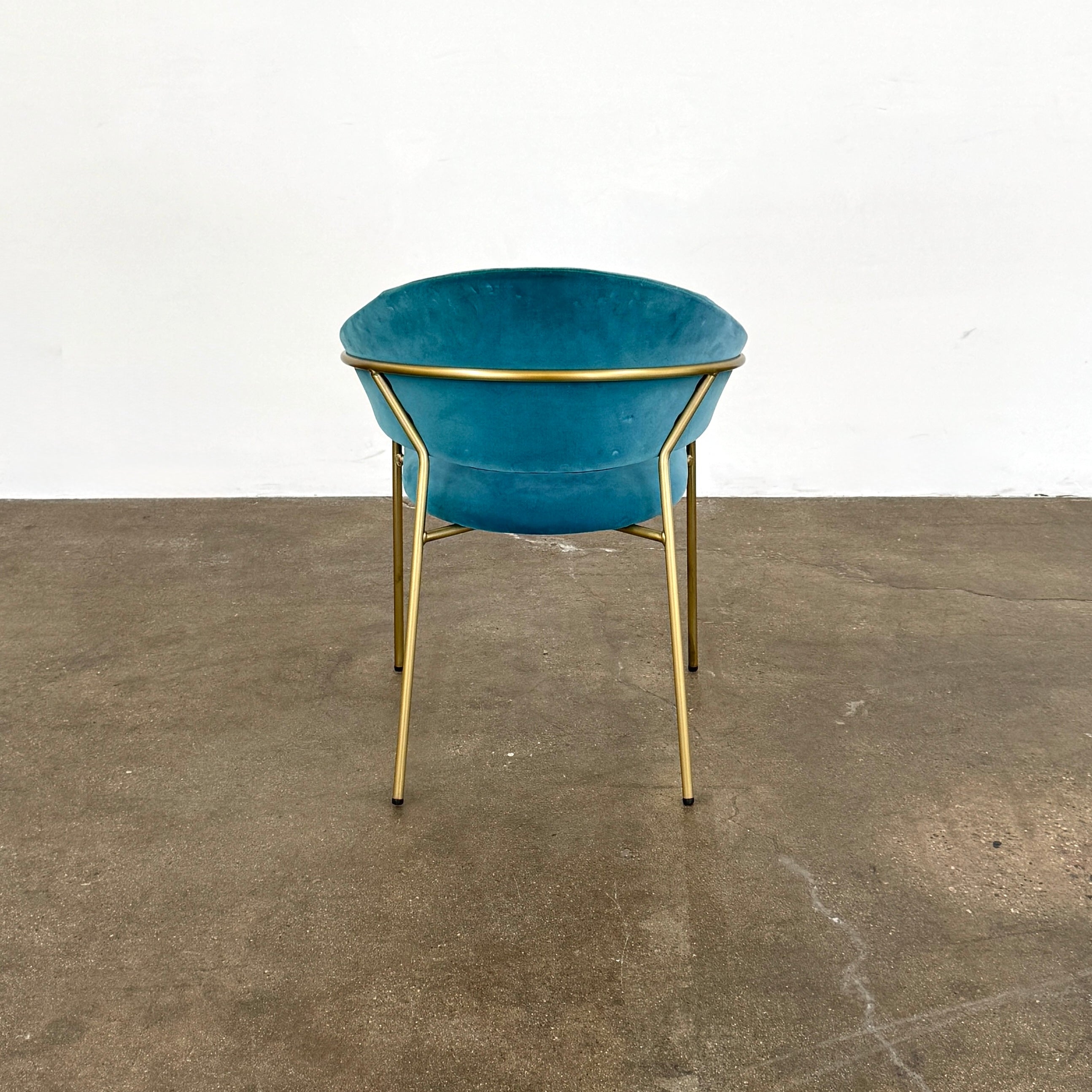Two Pedrali Jazz Chairs by Pedrali, featuring customizable teal velvet upholstery and gold metal legs, sit side by side on a concrete floor against a white wall, highlighting their stylish steel structure.