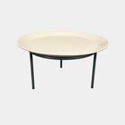 The Gervasoni Brise 54 Outdoor Coffee Table by Gervasoni features a round beige tray top and three black metal legs, shown against a light grey background—perfect for adding modern style to outdoor spaces.