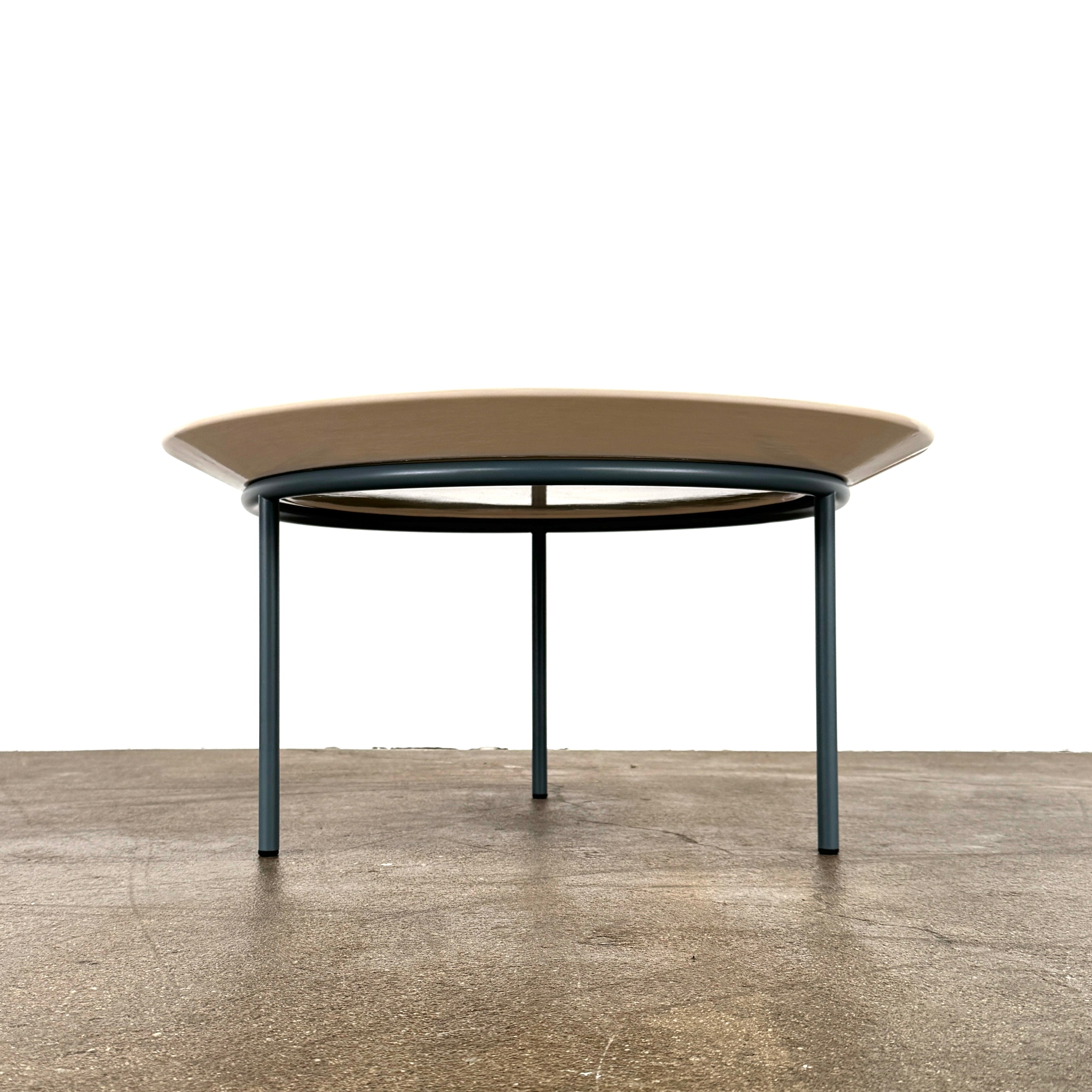 The Gervasoni Brise 54 Outdoor Coffee Table by Gervasoni features a round beige tray top and three black metal legs, shown against a light grey background—perfect for adding modern style to outdoor spaces.