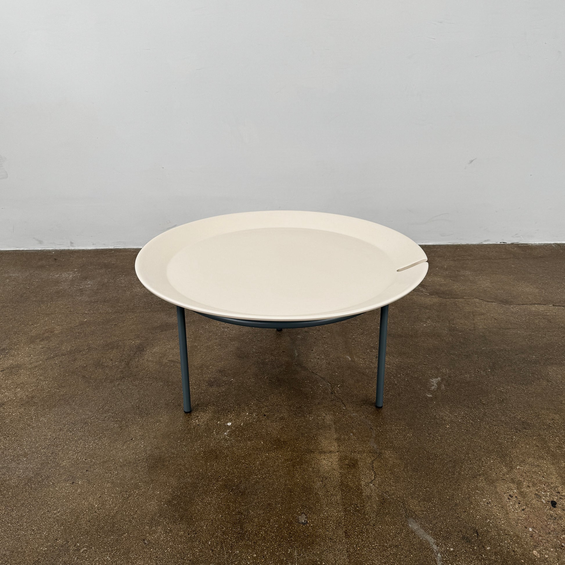 The Gervasoni Brise 54 Outdoor Coffee Table by Gervasoni features a round beige tray top and three black metal legs, shown against a light grey background—perfect for adding modern style to outdoor spaces.