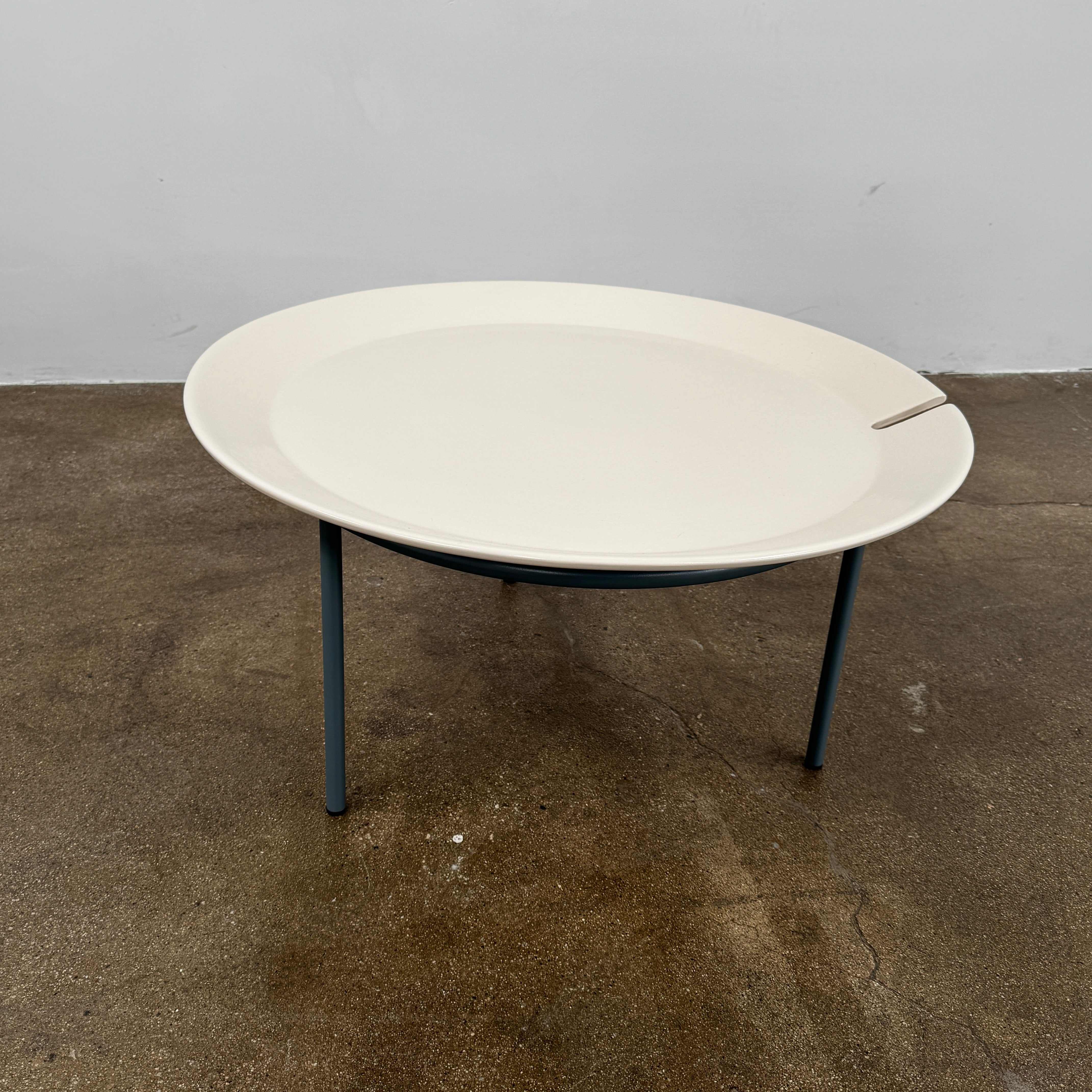 The Gervasoni Brise 54 Outdoor Coffee Table by Gervasoni features a round beige tray top and three black metal legs, shown against a light grey background—perfect for adding modern style to outdoor spaces.