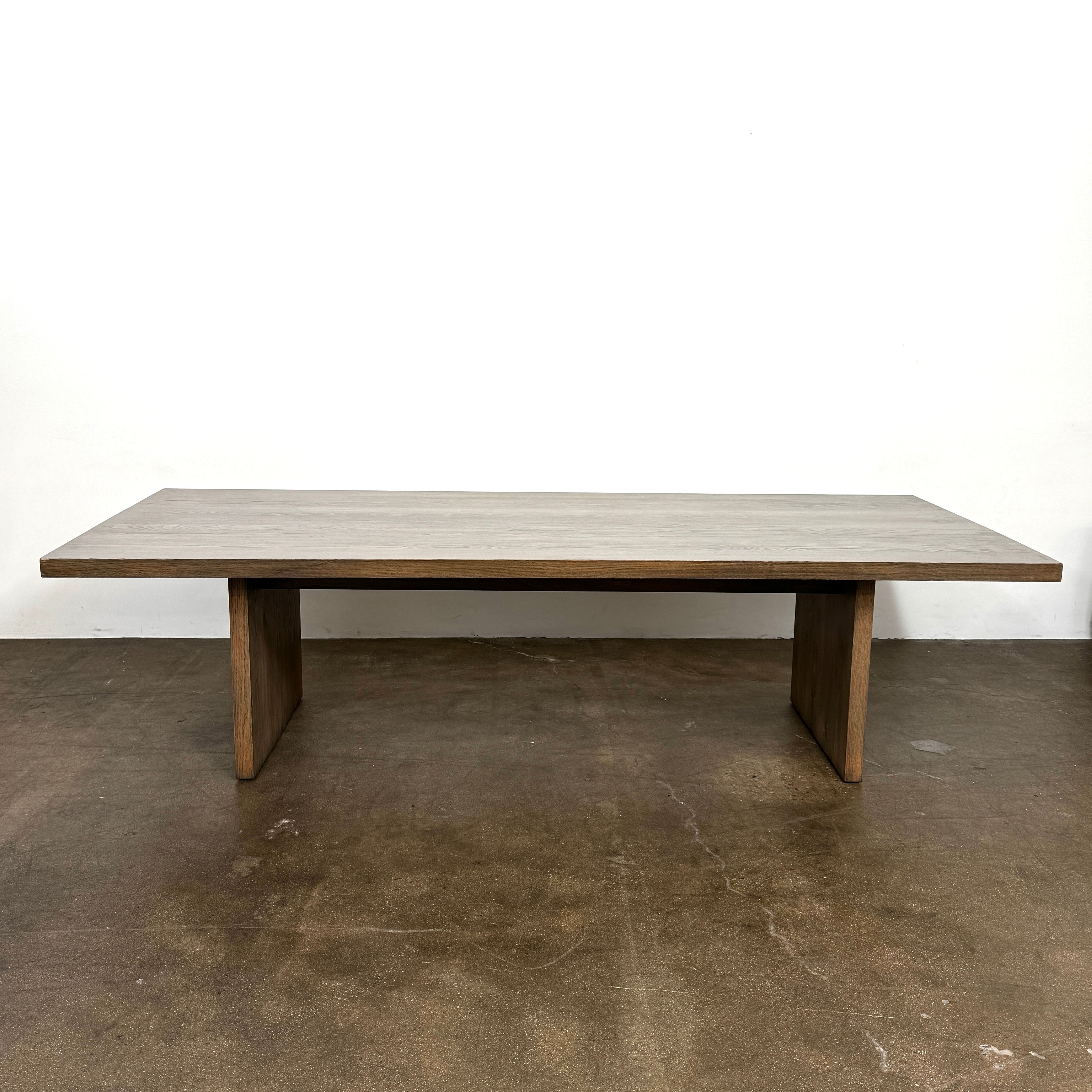 The BDDW Solid Oak dining table by BDDW features a simple, modern rectangular design and is set against a plain white wall on a polished concrete floor.