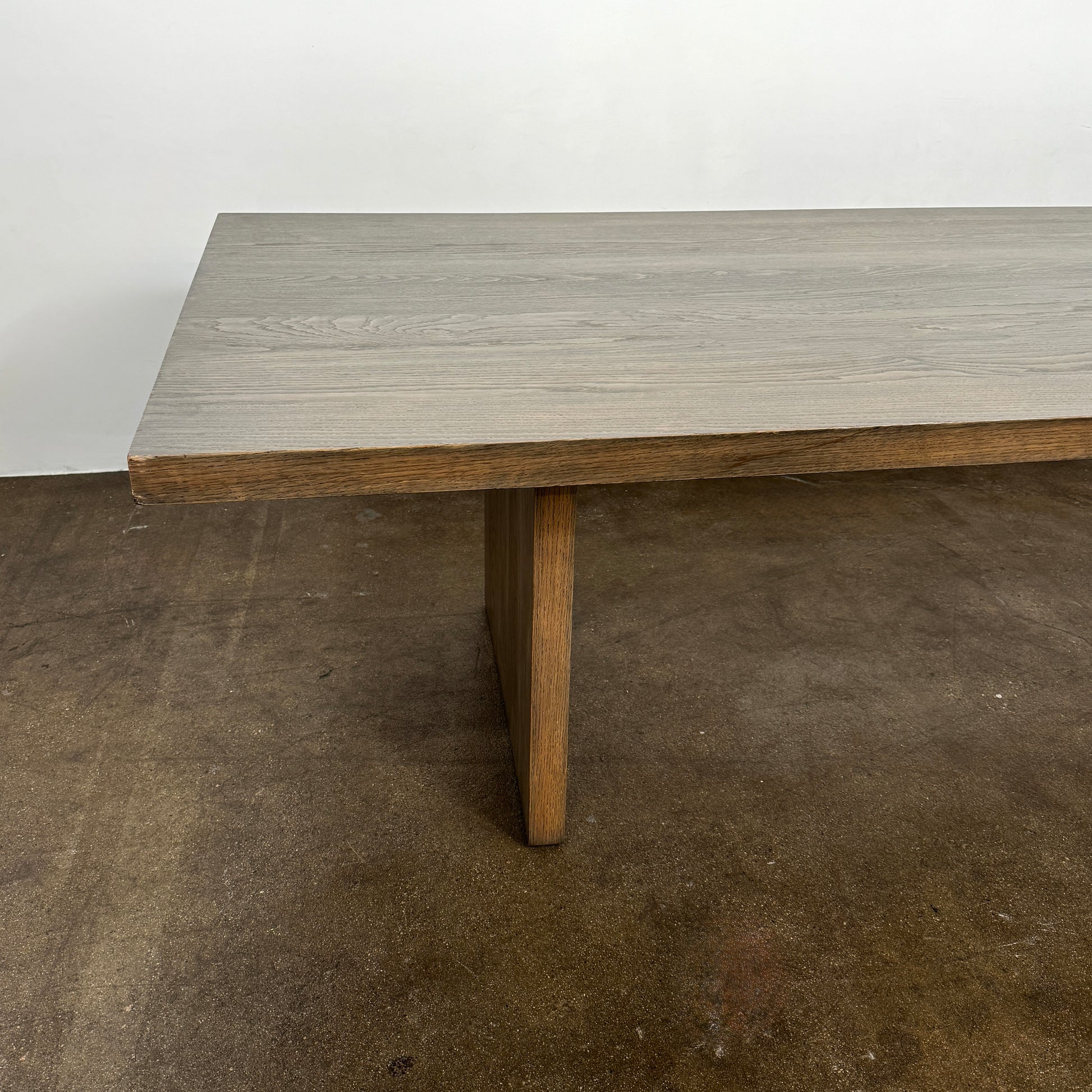 The BDDW Solid Oak dining table by BDDW features a simple, modern rectangular design and is set against a plain white wall on a polished concrete floor.
