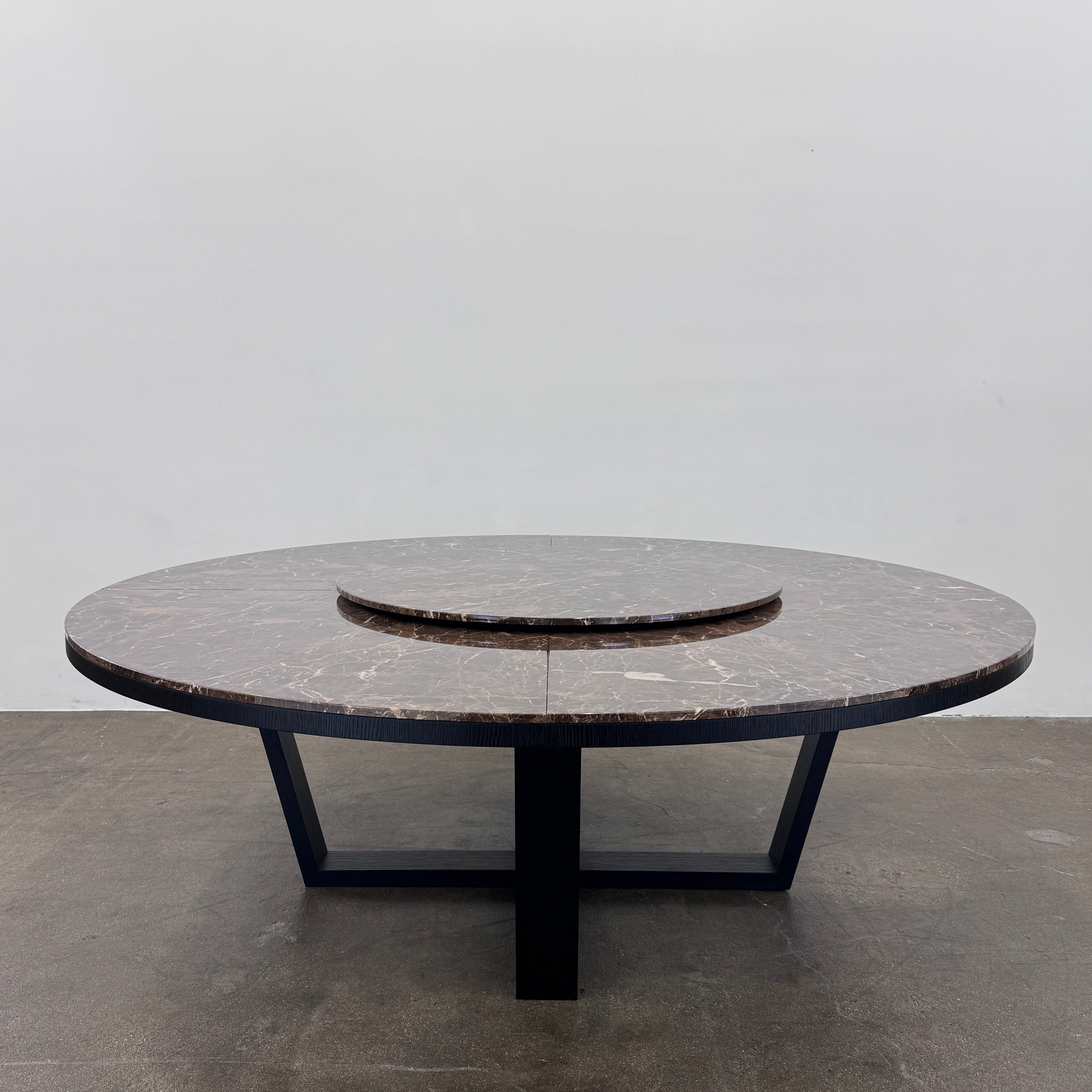 The Maxalto Xilos Dining Table with Rotating Tray by Maxalto features a round, dark finish and a black geometric base, shown here against a plain light background.