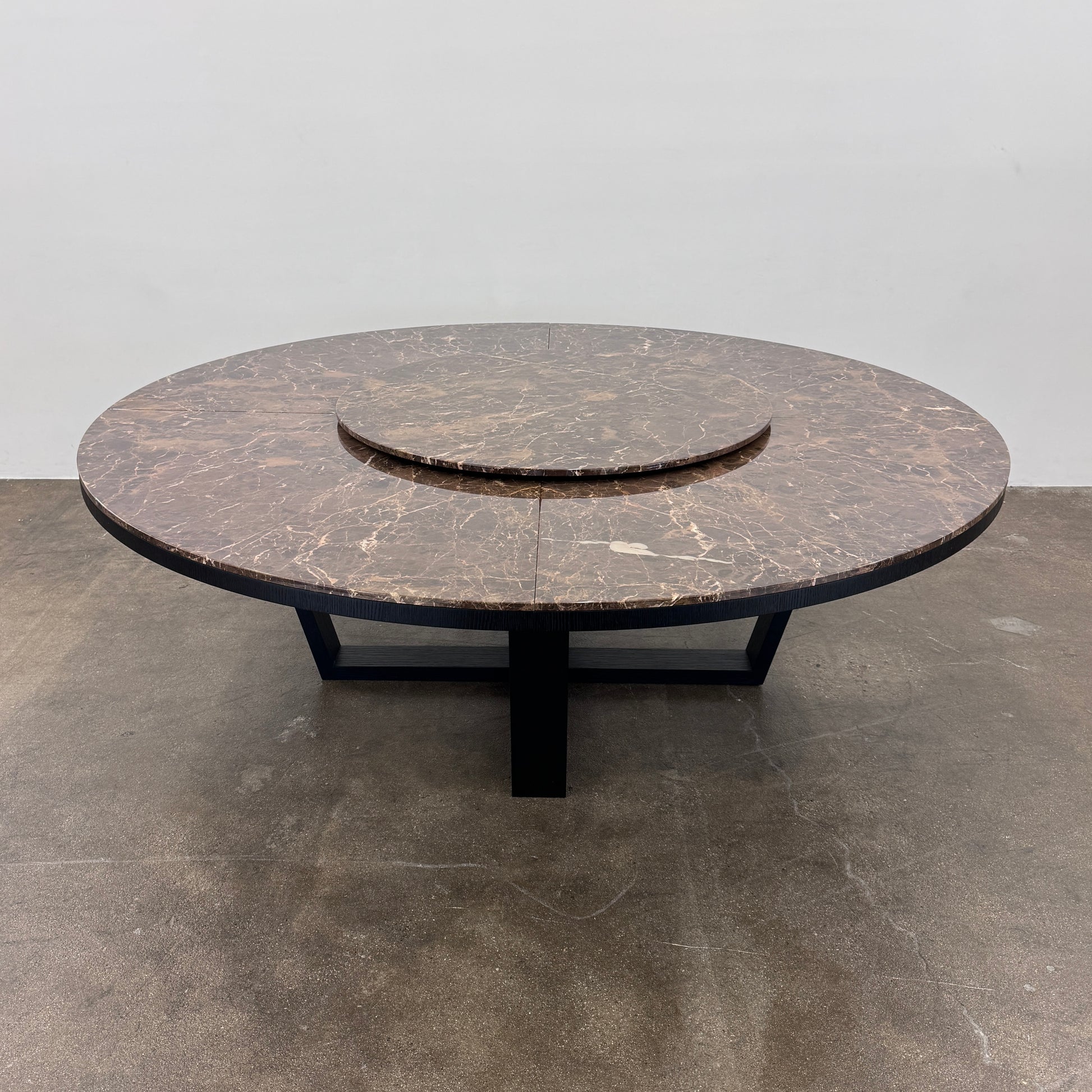 The Maxalto Xilos Dining Table with Rotating Tray by Maxalto features a round, dark finish and a black geometric base, shown here against a plain light background.