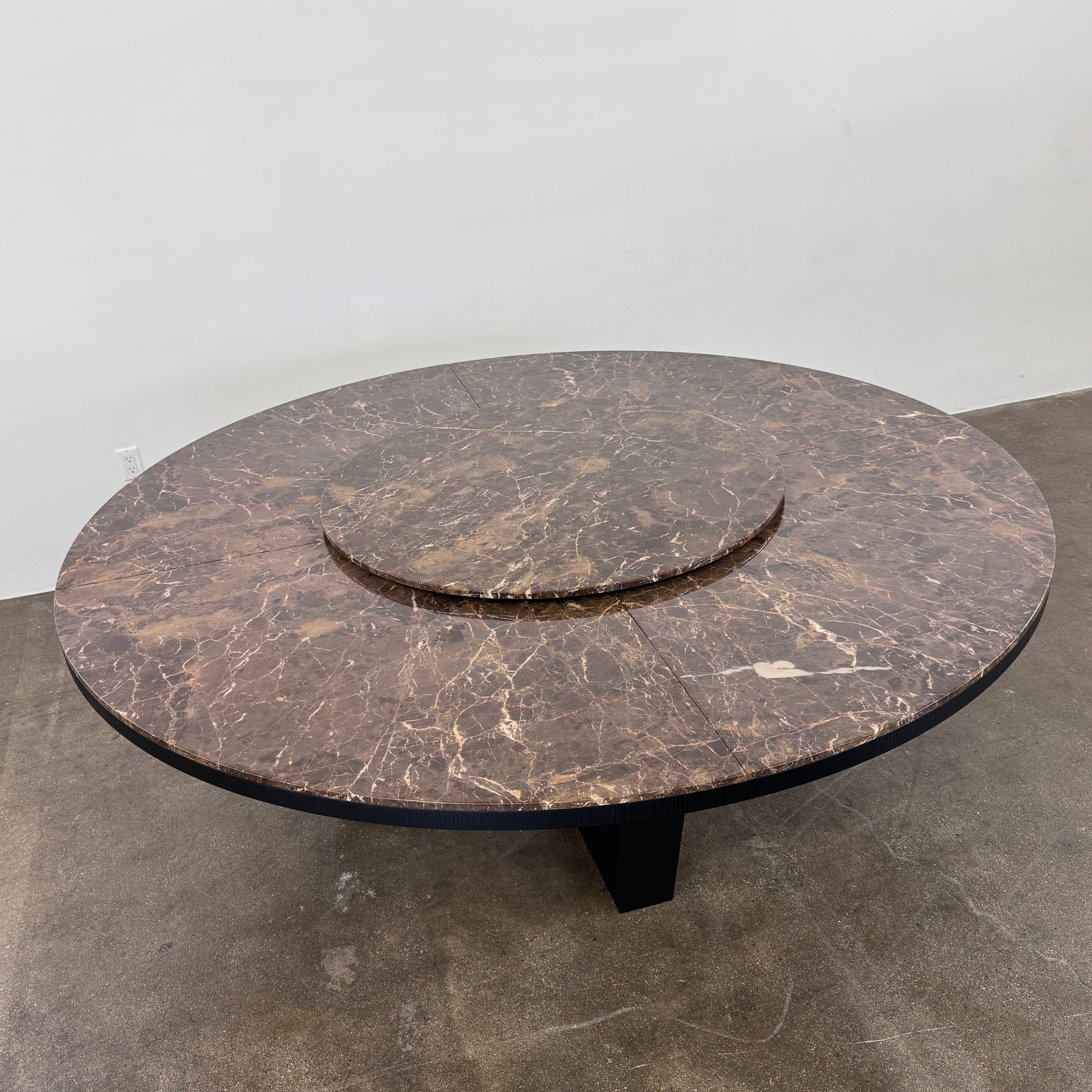 The Maxalto Xilos Dining Table with Rotating Tray by Maxalto features a round, dark finish and a black geometric base, shown here against a plain light background.