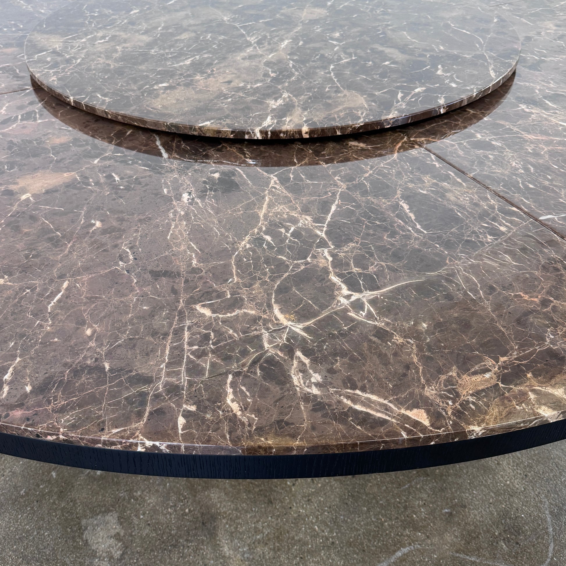 The Maxalto Xilos Dining Table with Rotating Tray by Maxalto features a round, dark finish and a black geometric base, shown here against a plain light background.