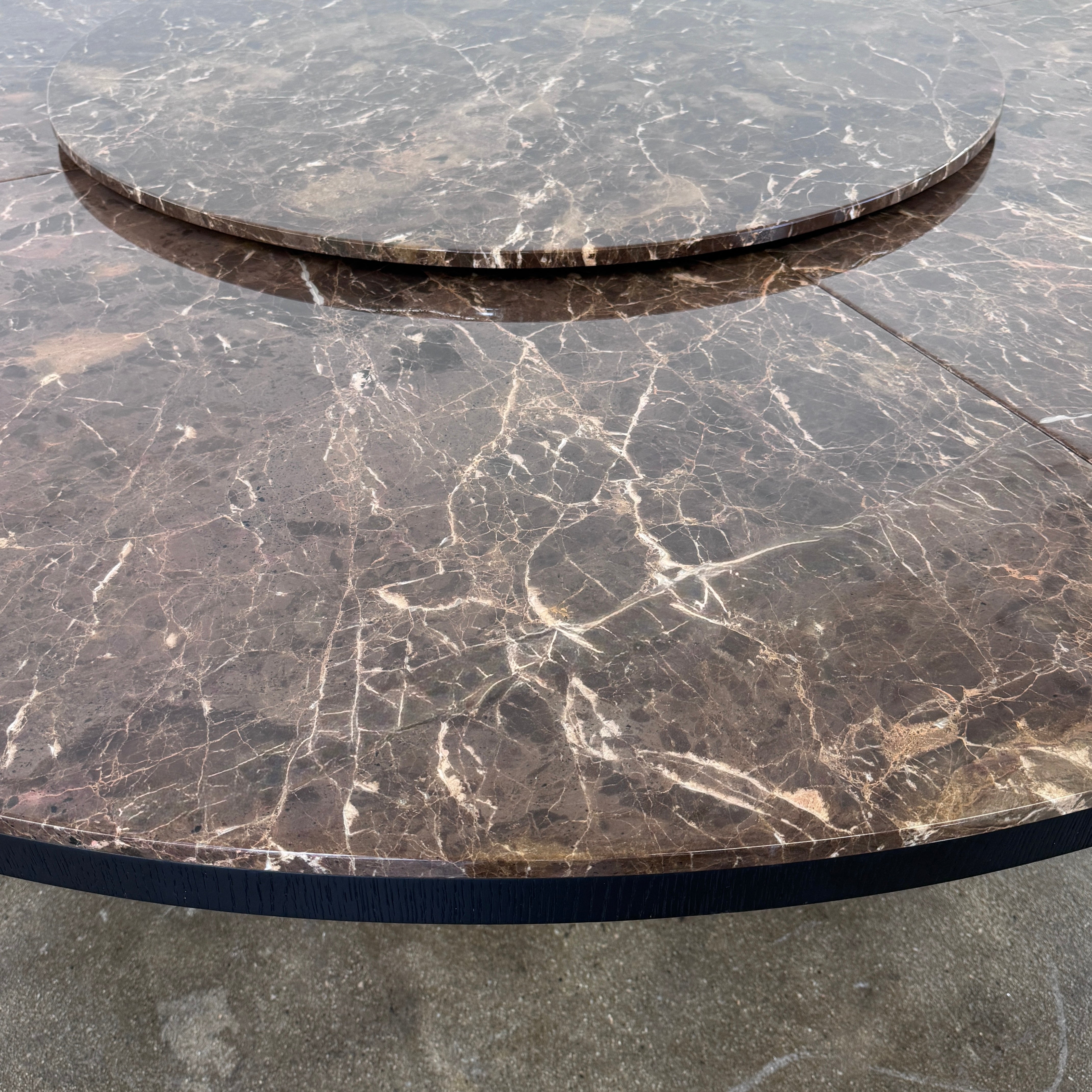 The Maxalto Xilos Dining Table with Rotating Tray by Maxalto features a round, dark finish and a black geometric base, shown here against a plain light background.