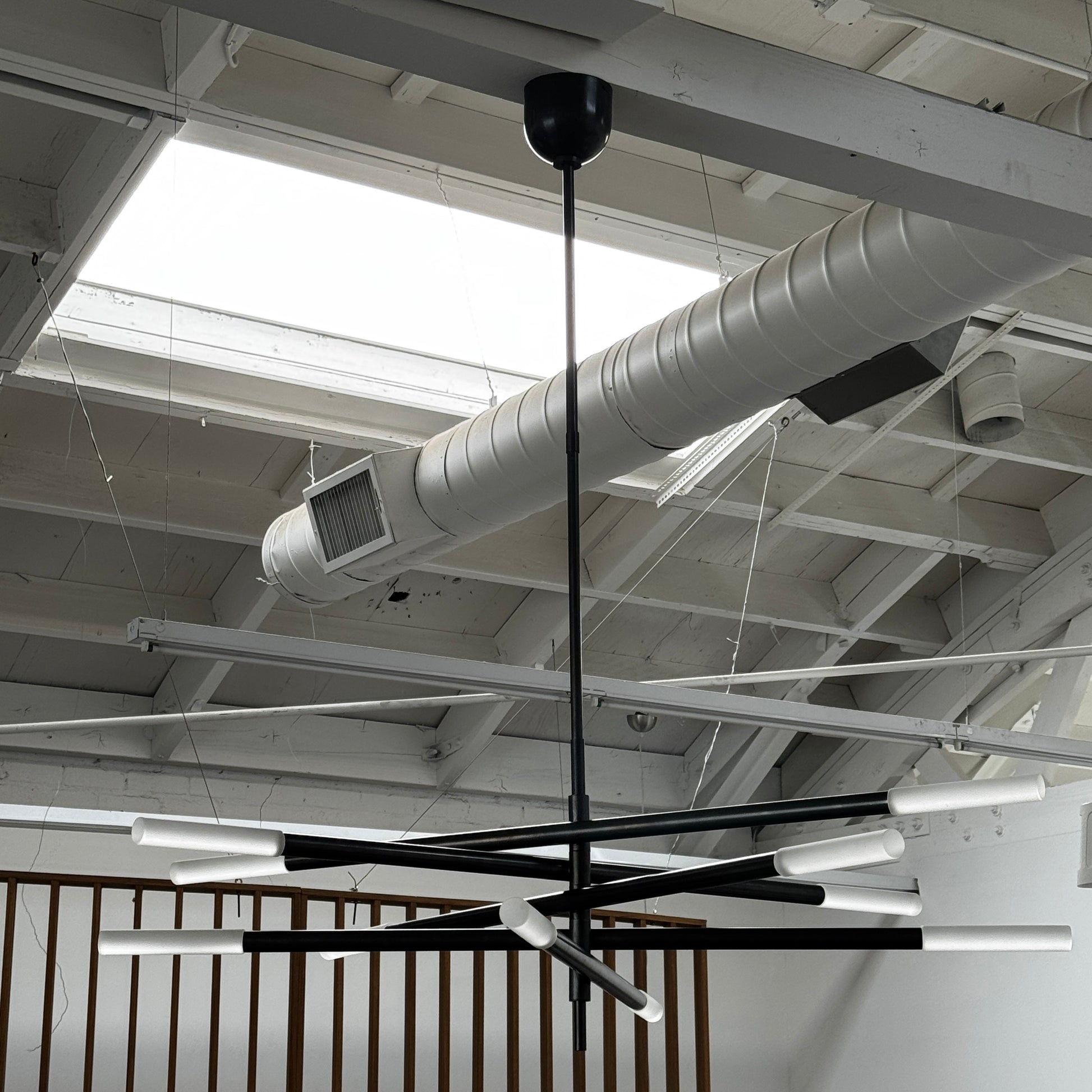 The Visual Comfort Signature Rousseau Grande Ten Light Articulating Chandelier features a modern black design with ten horizontal arms, each ending in a yellow-toned rectangular light, suspended from a central black rod against a white background.