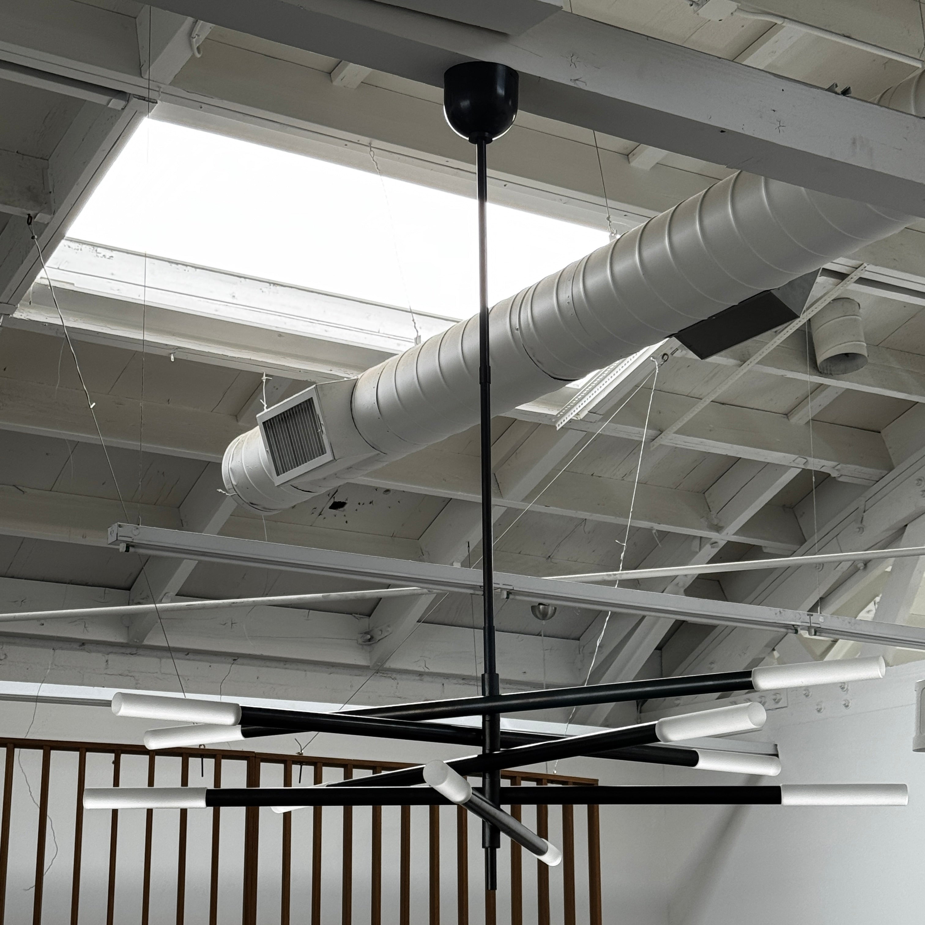 The Visual Comfort Signature Rousseau Grande Ten Light Articulating Chandelier features a modern black design with ten horizontal arms, each ending in a yellow-toned rectangular light, suspended from a central black rod against a white background.