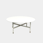 The MillerKnoll Sommer Outdoor Coffee Table for DWR is a round, white table with four legs and an X-shaped base, ideal for minimalist outdoor spaces. Brand: MillerKnoll. Set against a plain white background.