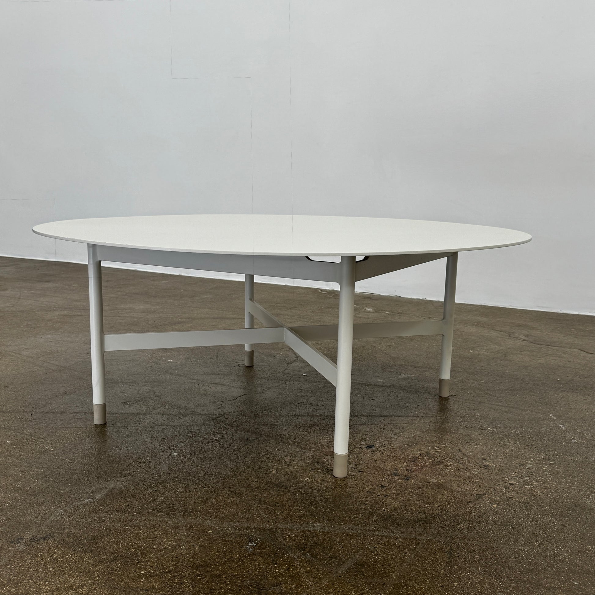 The MillerKnoll Sommer Outdoor Coffee Table for DWR is a round, white table with four legs and an X-shaped base, ideal for minimalist outdoor spaces. Brand: MillerKnoll. Set against a plain white background.