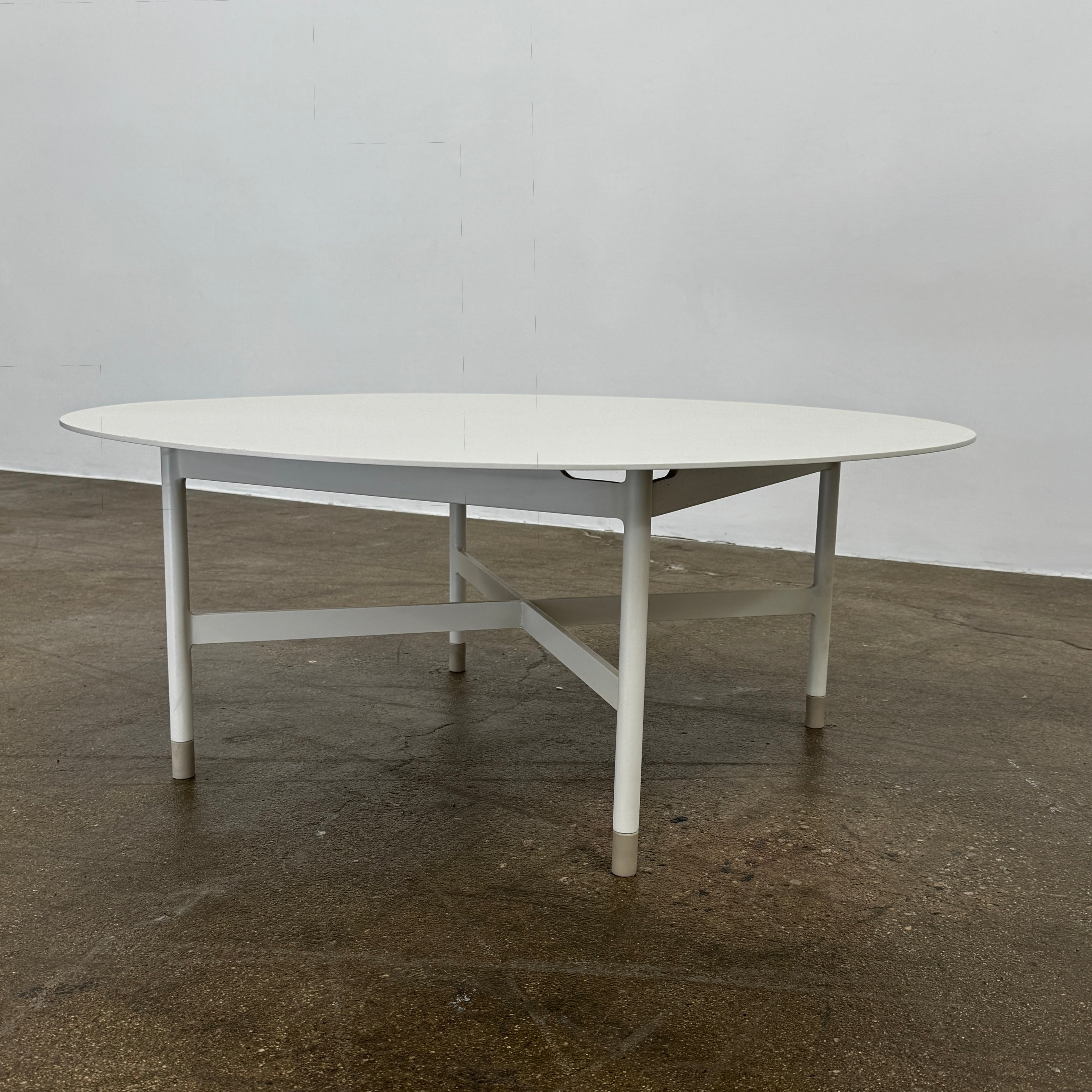 The MillerKnoll Sommer Outdoor Coffee Table for DWR is a round, white table with four legs and an X-shaped base, ideal for minimalist outdoor spaces. Brand: MillerKnoll. Set against a plain white background.