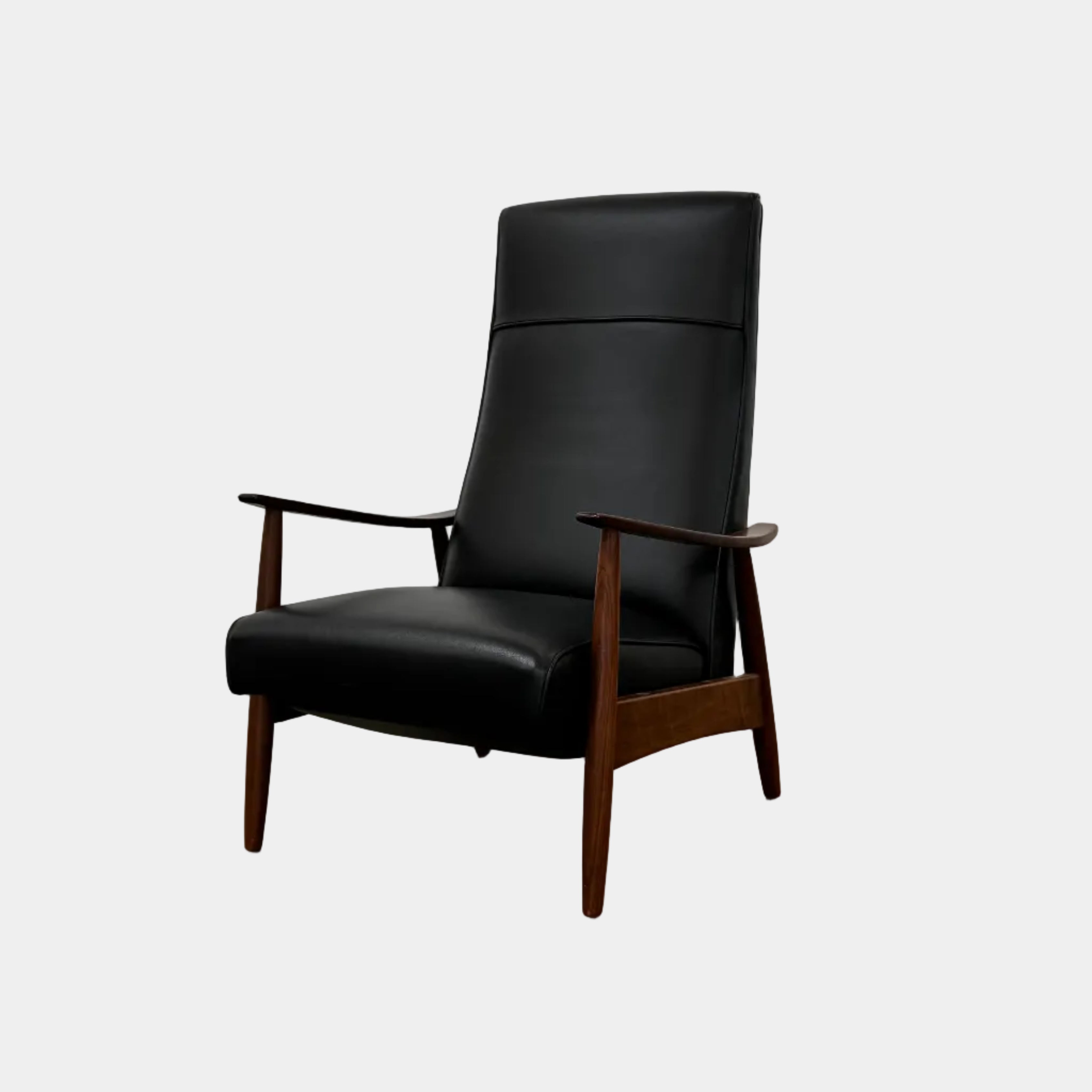The Thayer Coggin Milo Baughman Recliner 74, featuring a black leather seat and solid walnut frame with wooden arms and legs, sits on a bare concrete floor against a plain white wall.