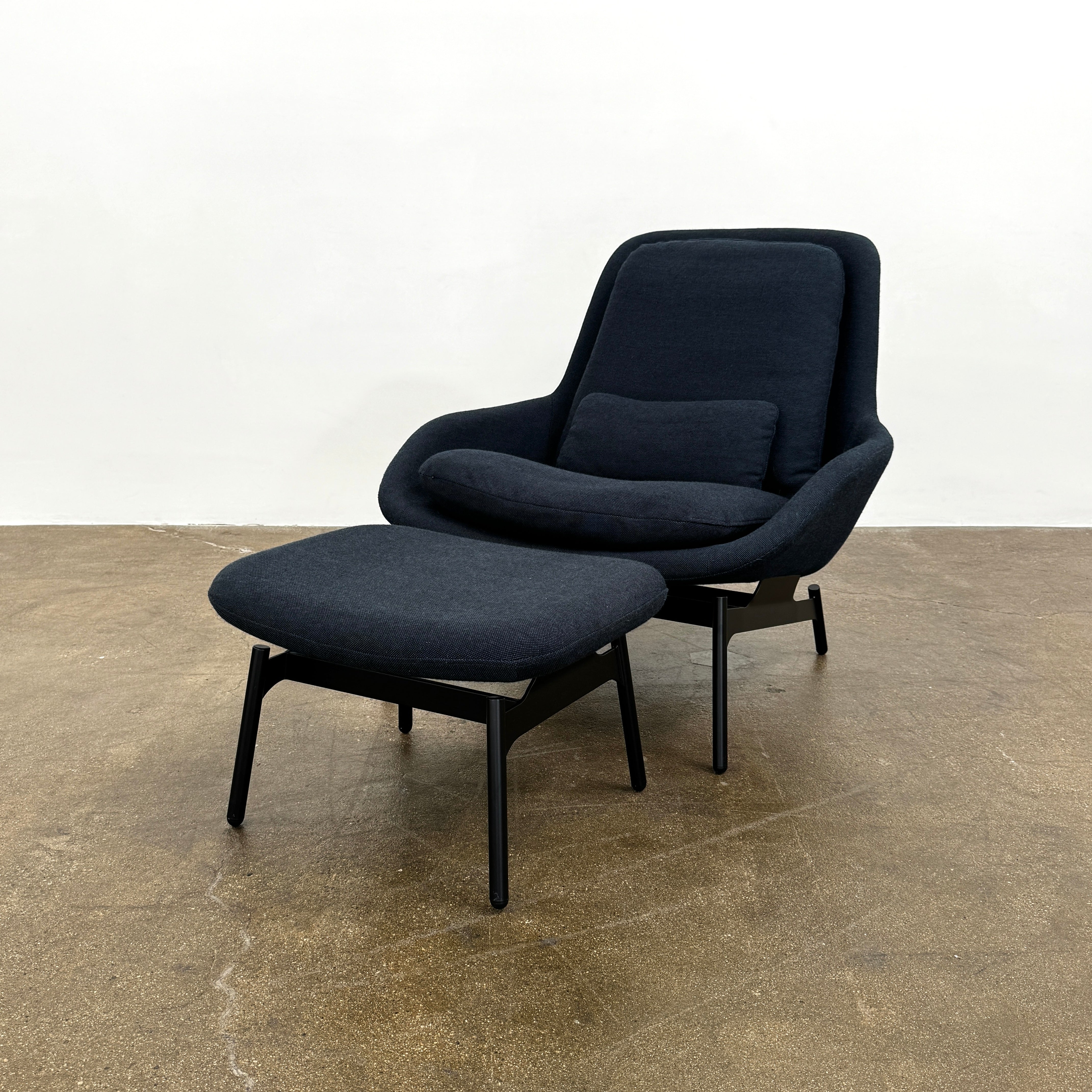 A Bludot Field Chair & Ottoman by Blu Dot, in modern black, is placed on a brown concrete floor with a white background.