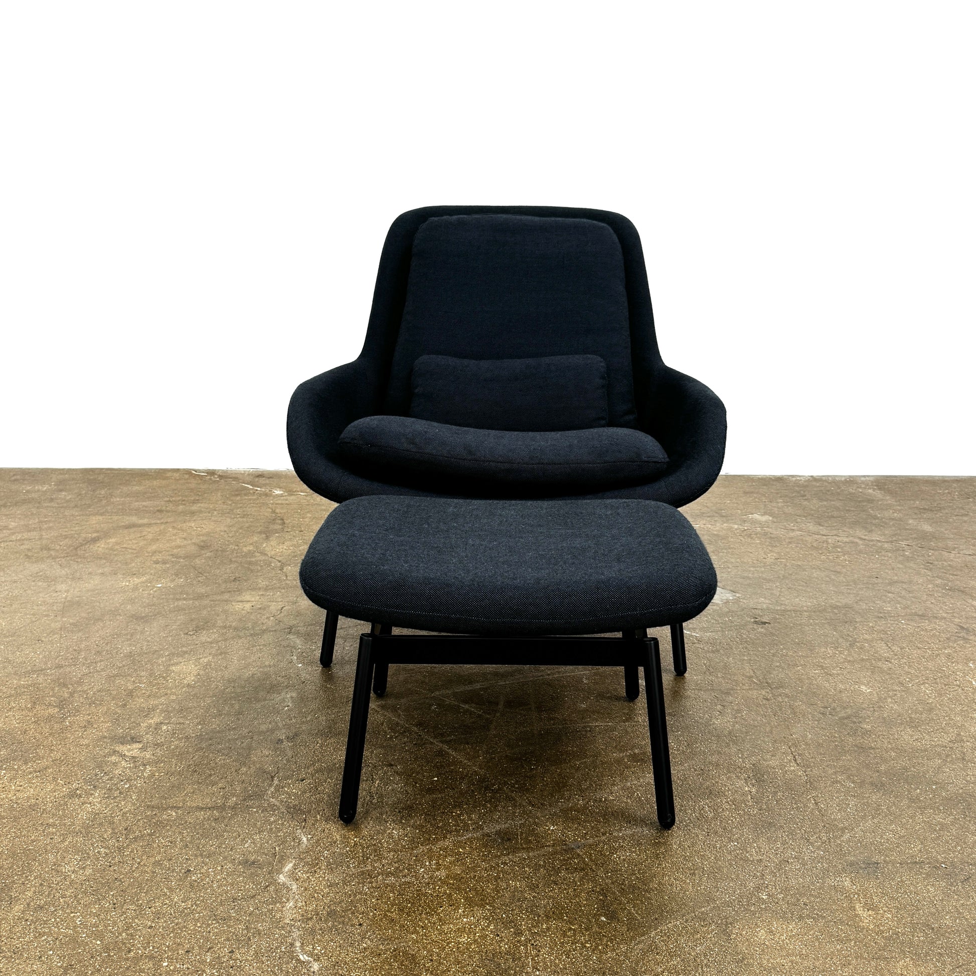 A Bludot Field Chair & Ottoman by Blu Dot, in modern black, is placed on a brown concrete floor with a white background.